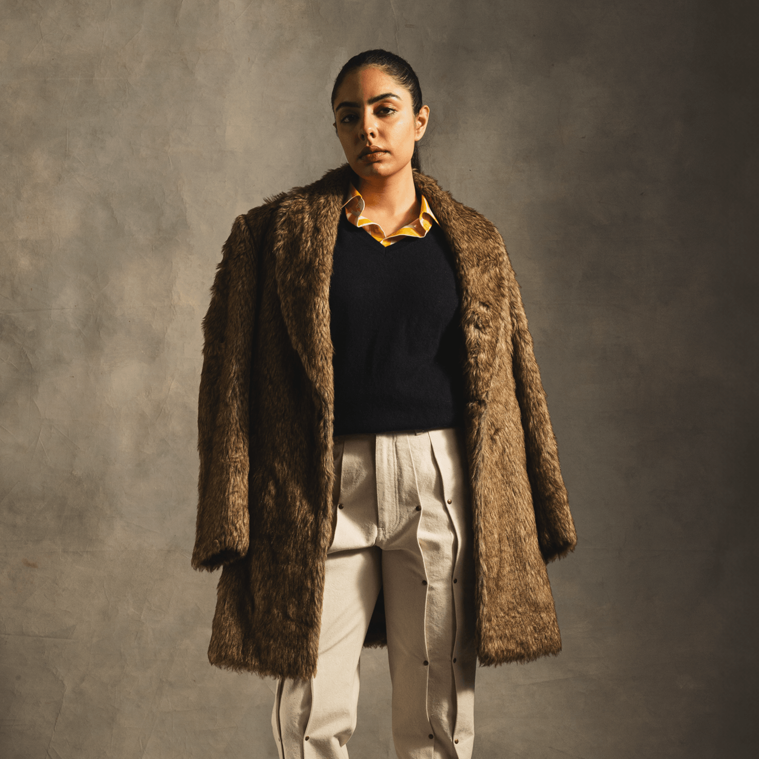 Woman modeling oversized brown faux fur coat with black sweater and beige pants