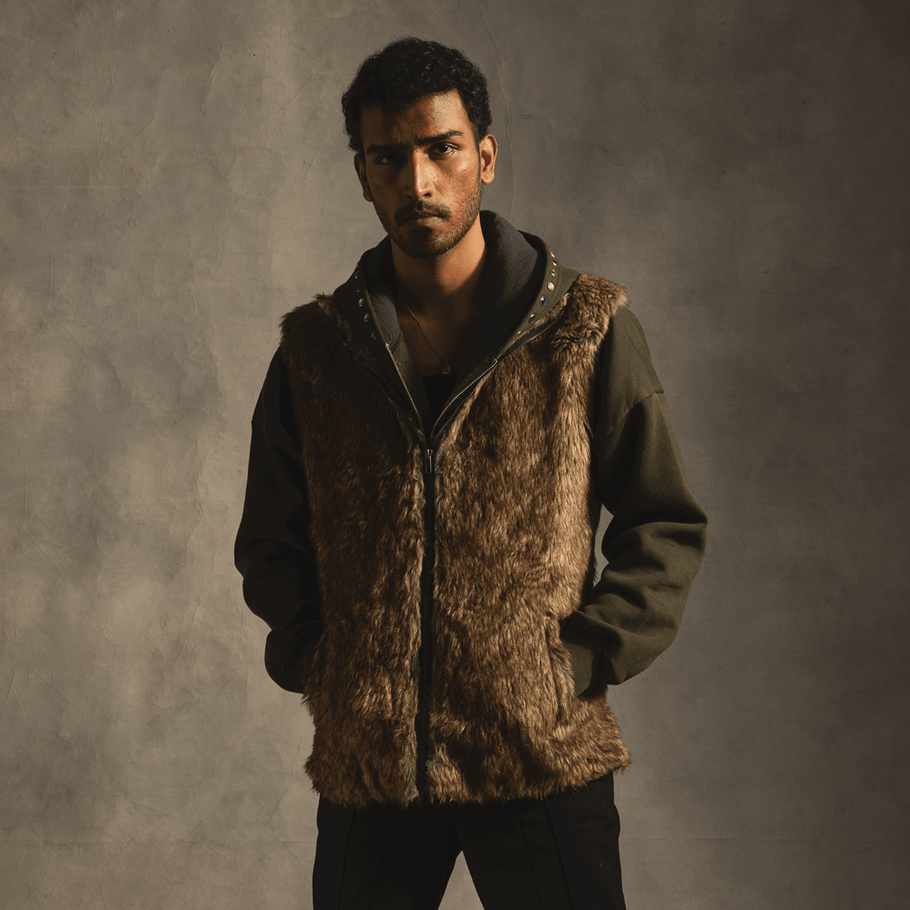 Man wearing brown faux fur vest over olive green hoodie, streetwear fashion