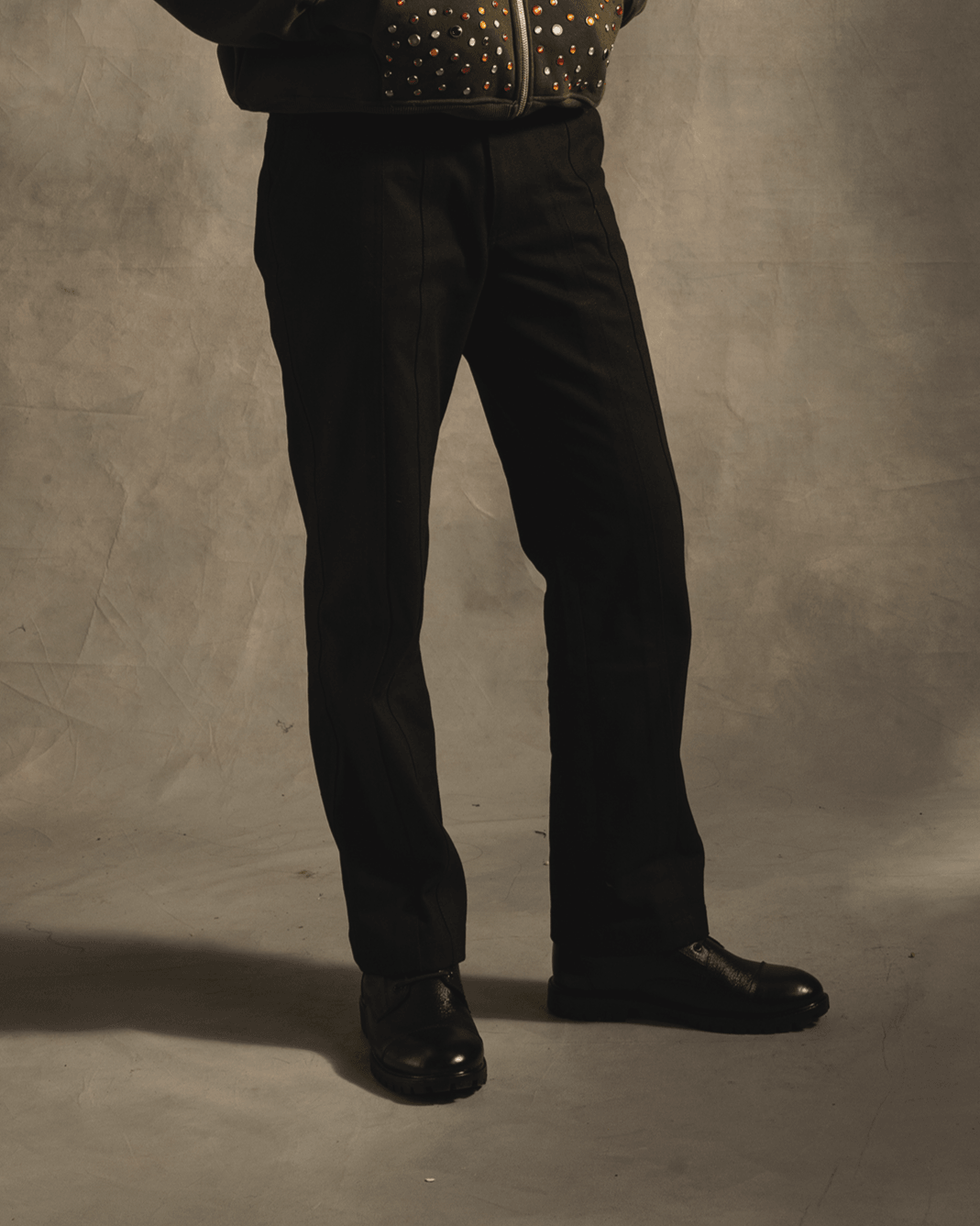 Black straight-leg pants and black shoes styled with a studded dark jacket, streetwear fashion