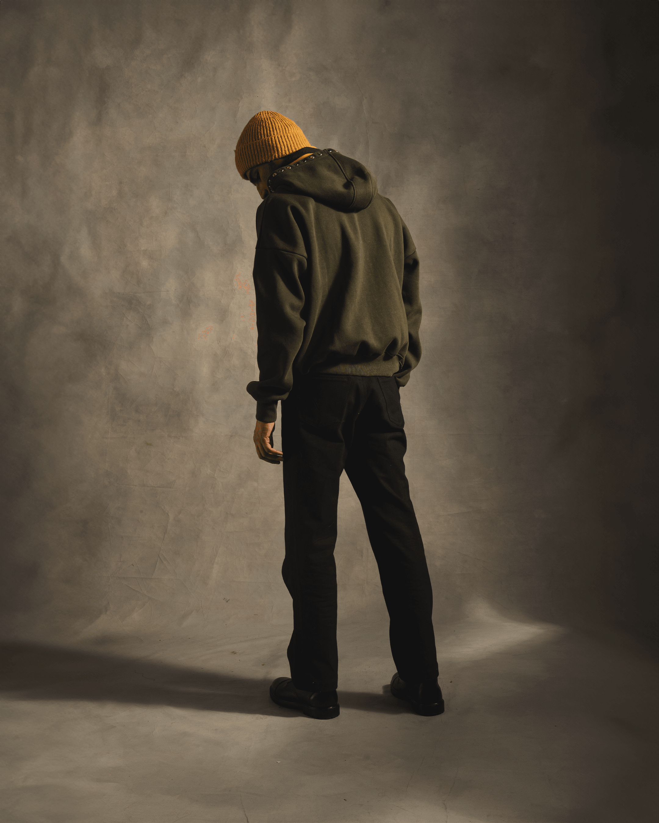 Man in olive green hoodie and yellow beanie standing in studio, streetwear fashion