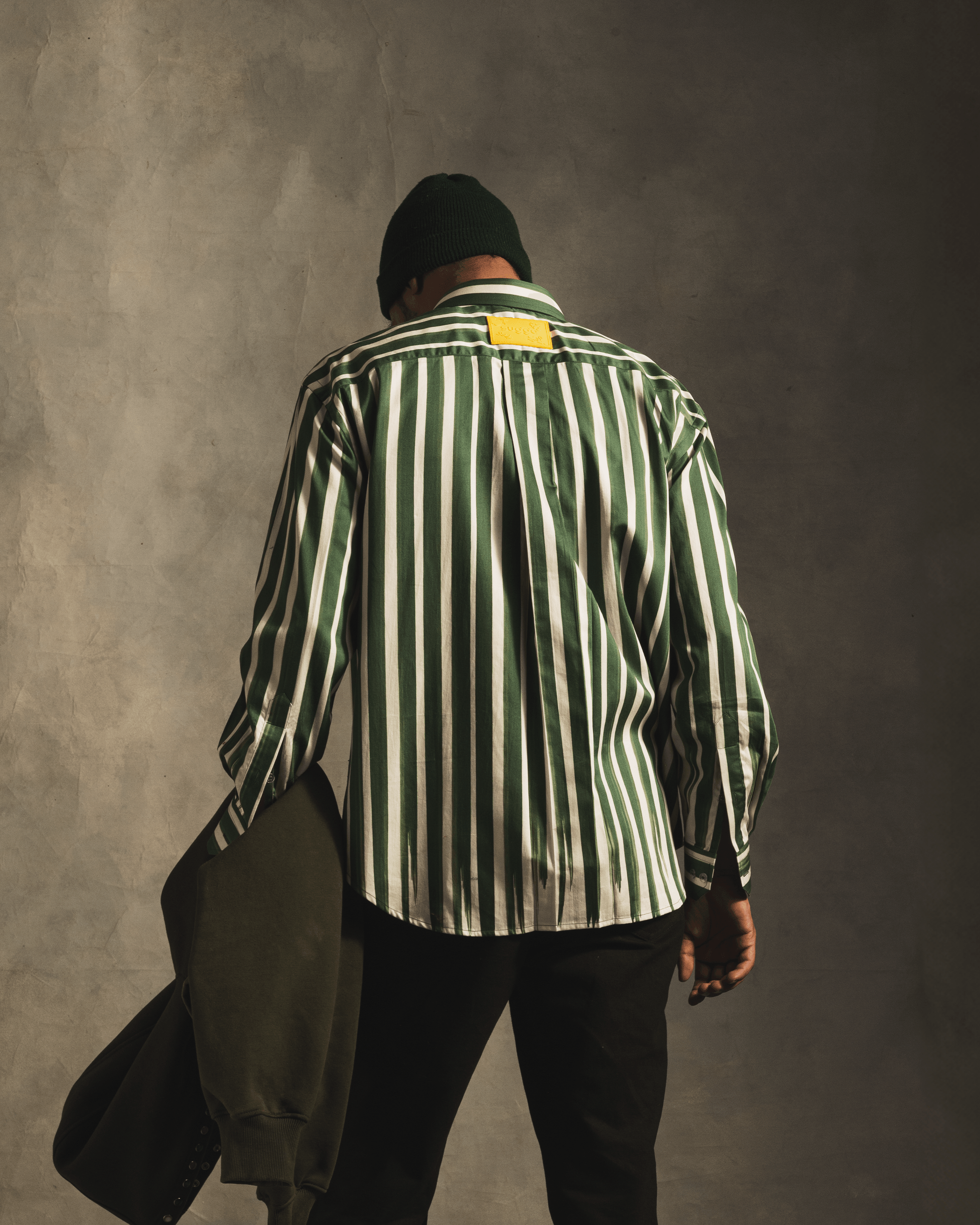 Man in green and white vertical striped shirt, black pants, holding jacket, streetwear style