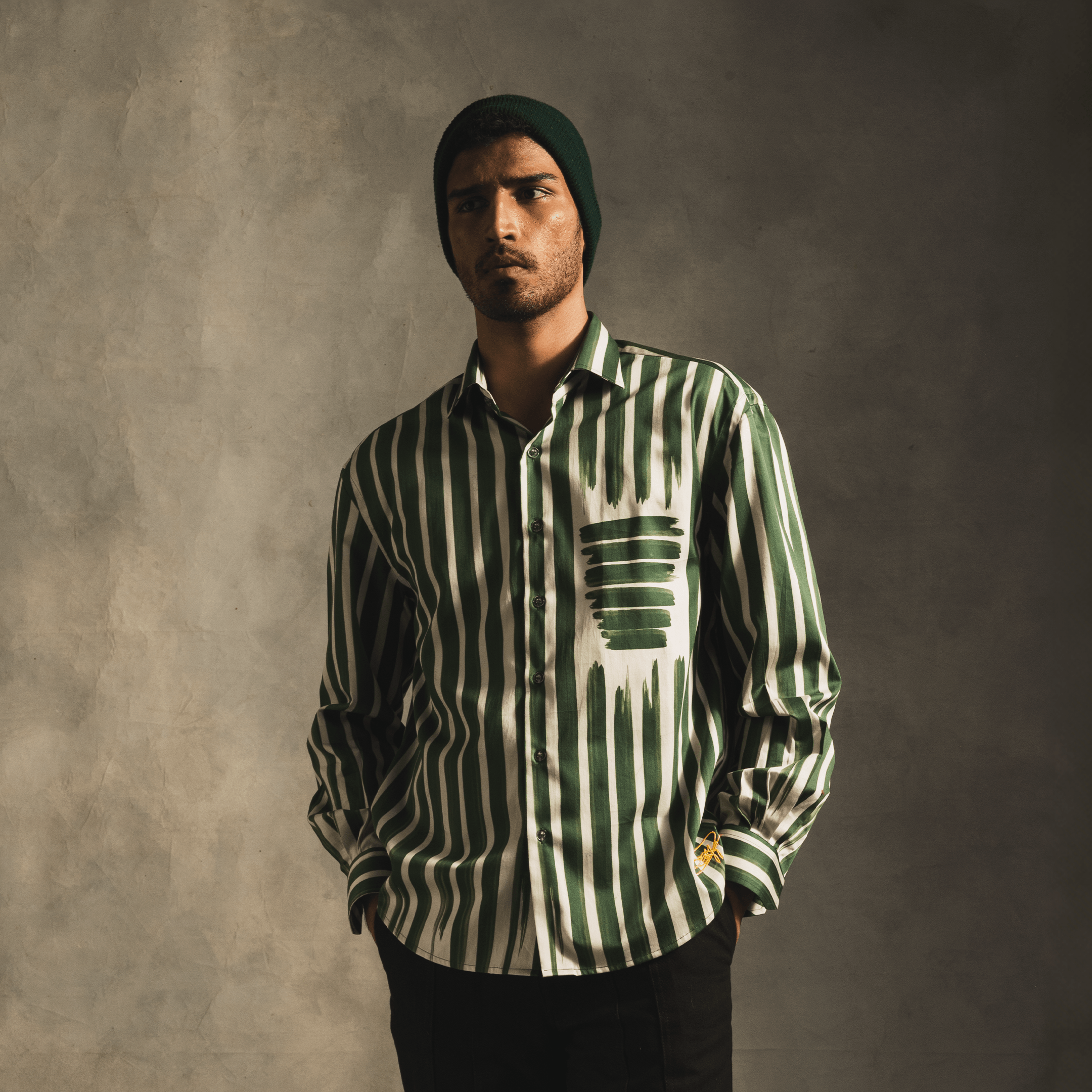 Man wearing green and white striped streetwear shirt with graphic pocket design and beanie.