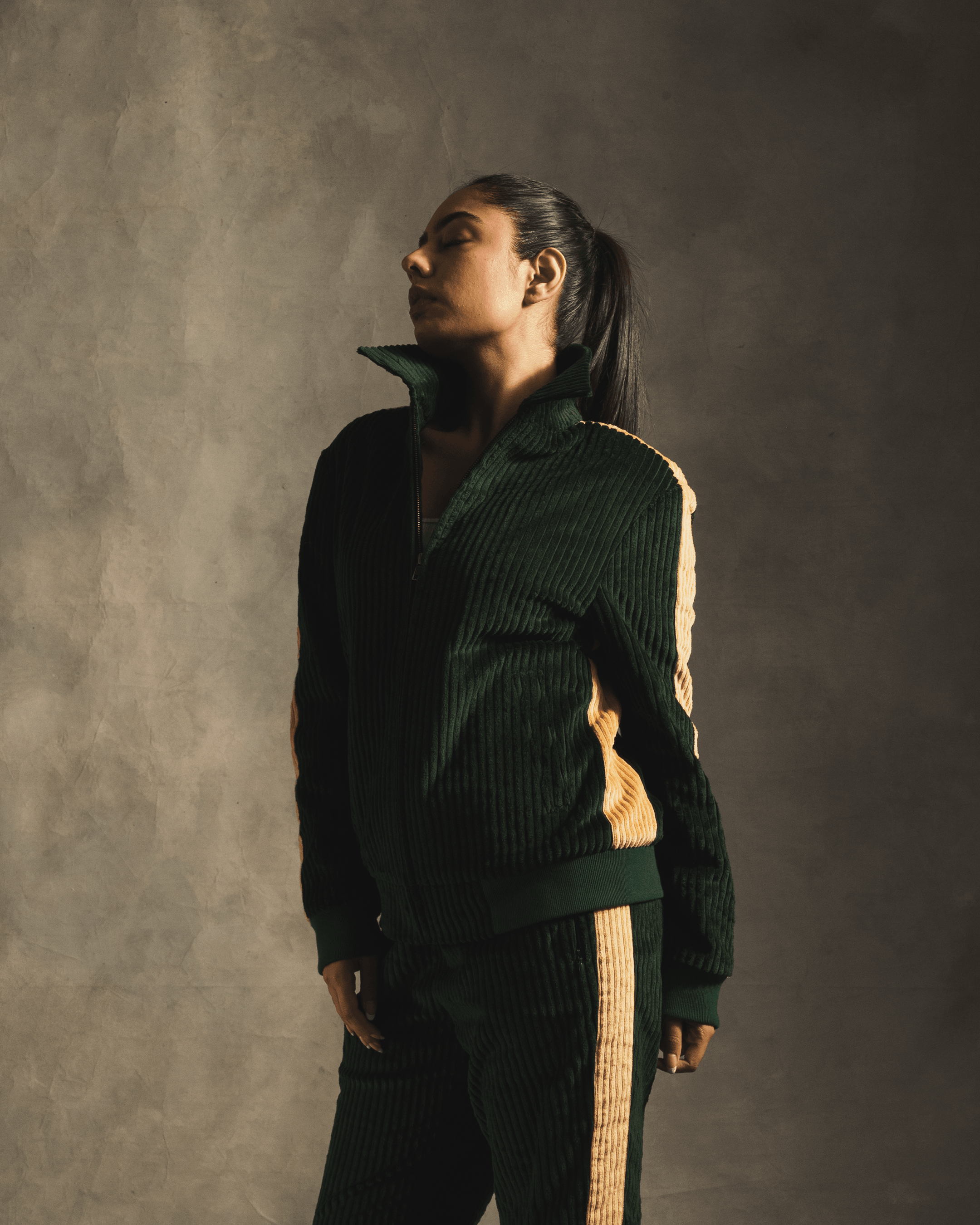 Woman wearing a green corduroy track jacket with yellow side stripes, streetwear fashion
