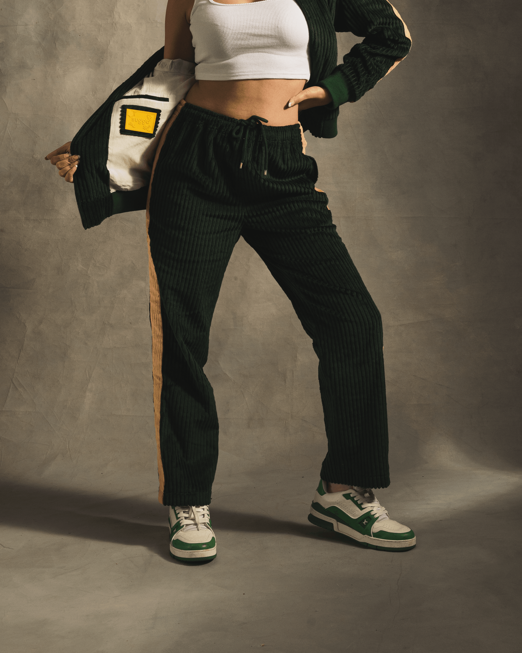 Model in dark green corduroy track pants with tan side stripes and green sneakers