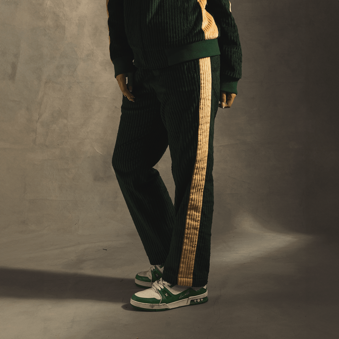Green corduroy track pants with yellow side stripes, styled with green and white sneakers