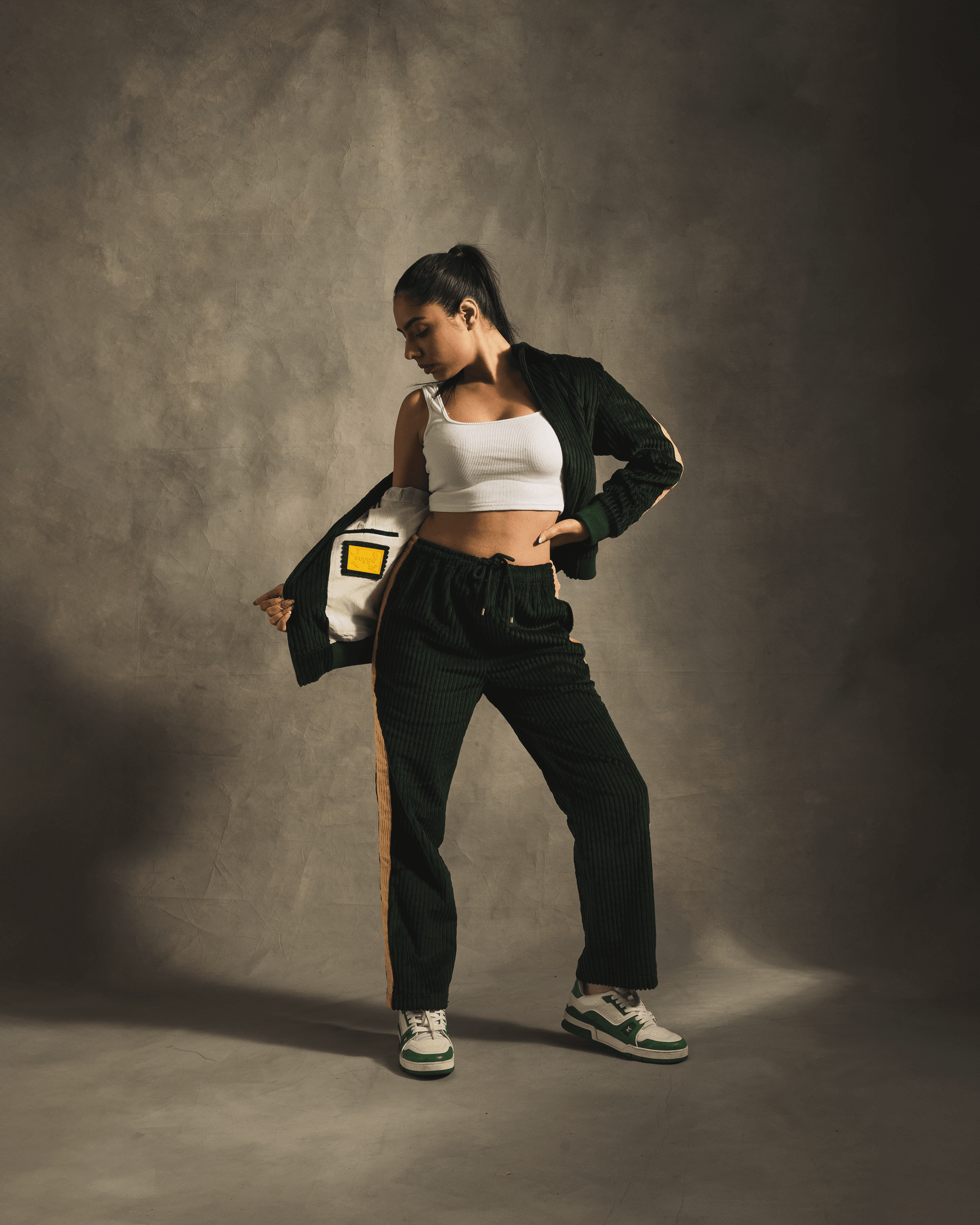 Woman wearing green corduroy tracksuit, white crop top, and trendy sneakers in studio