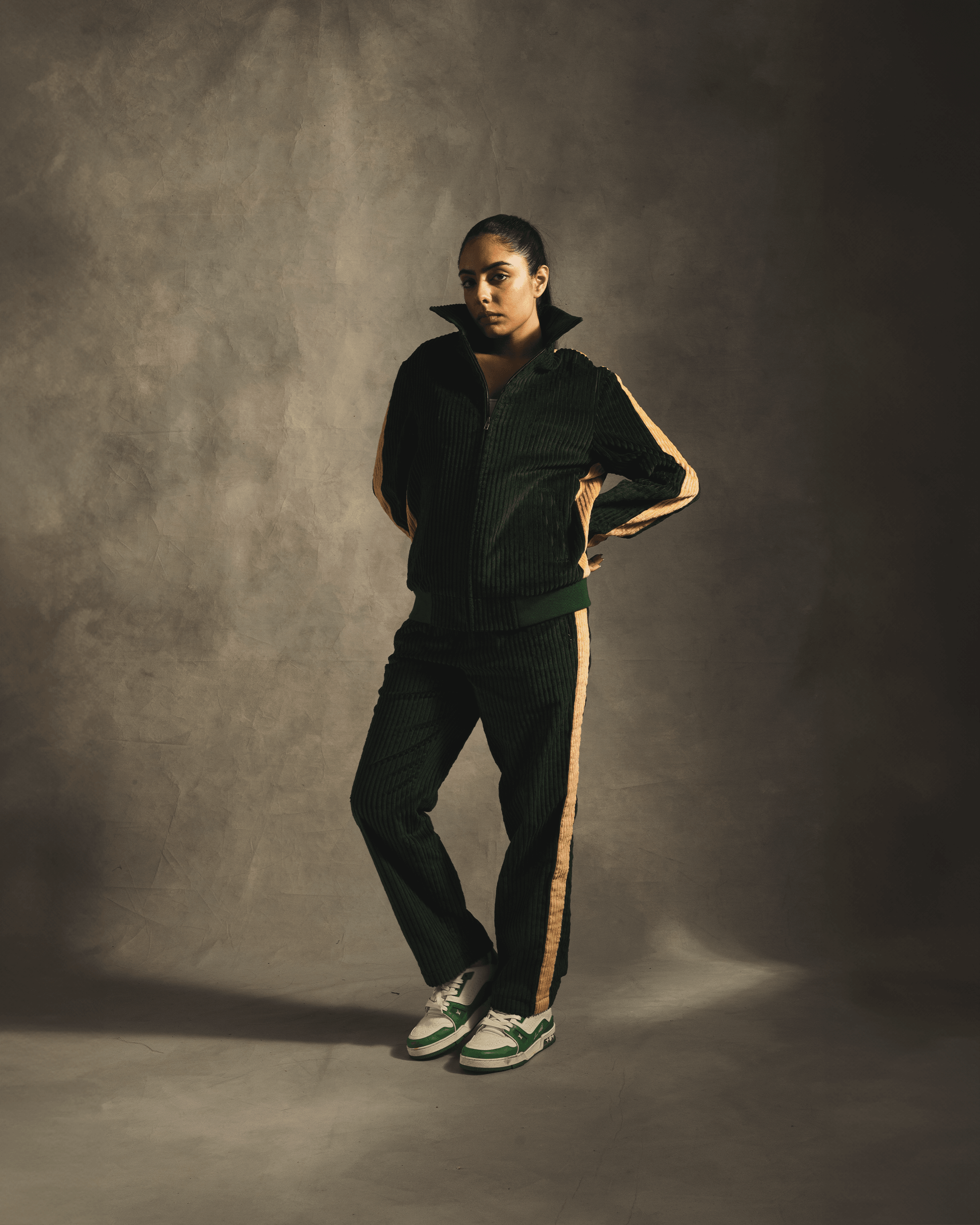 Woman in green corduroy tracksuit with tan side stripes and green sneakers, streetwear style
