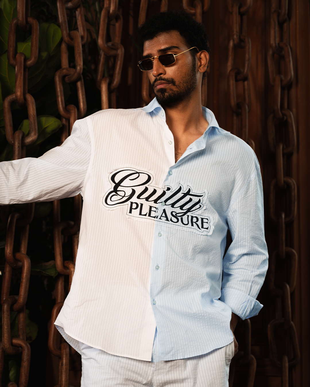 Man in sunglasses wearing a striped oversized shirt with 'Guilty Pleasure' text, streetwear fashion