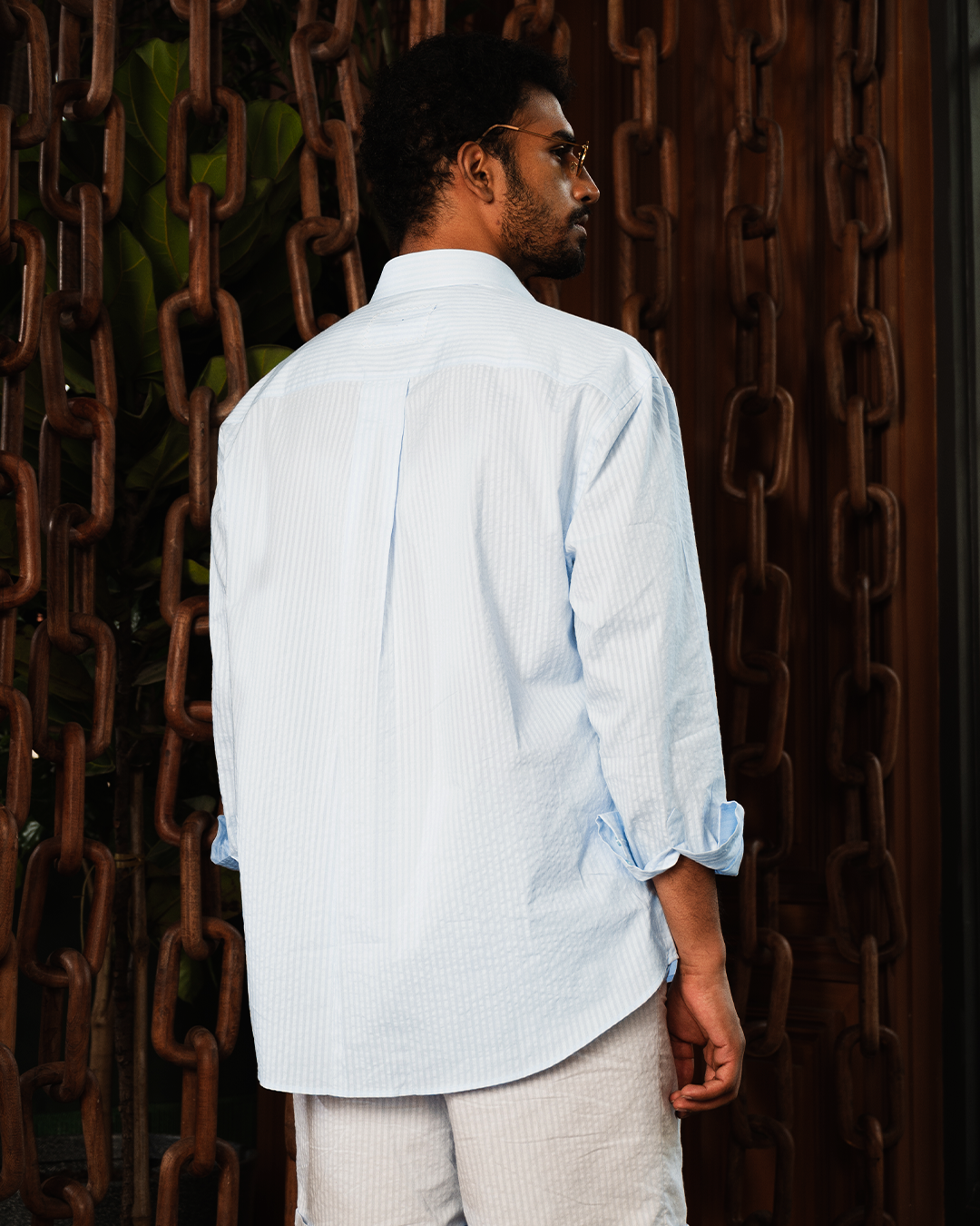 Man in light blue seersucker shirt and white shorts, standing near large metal chains