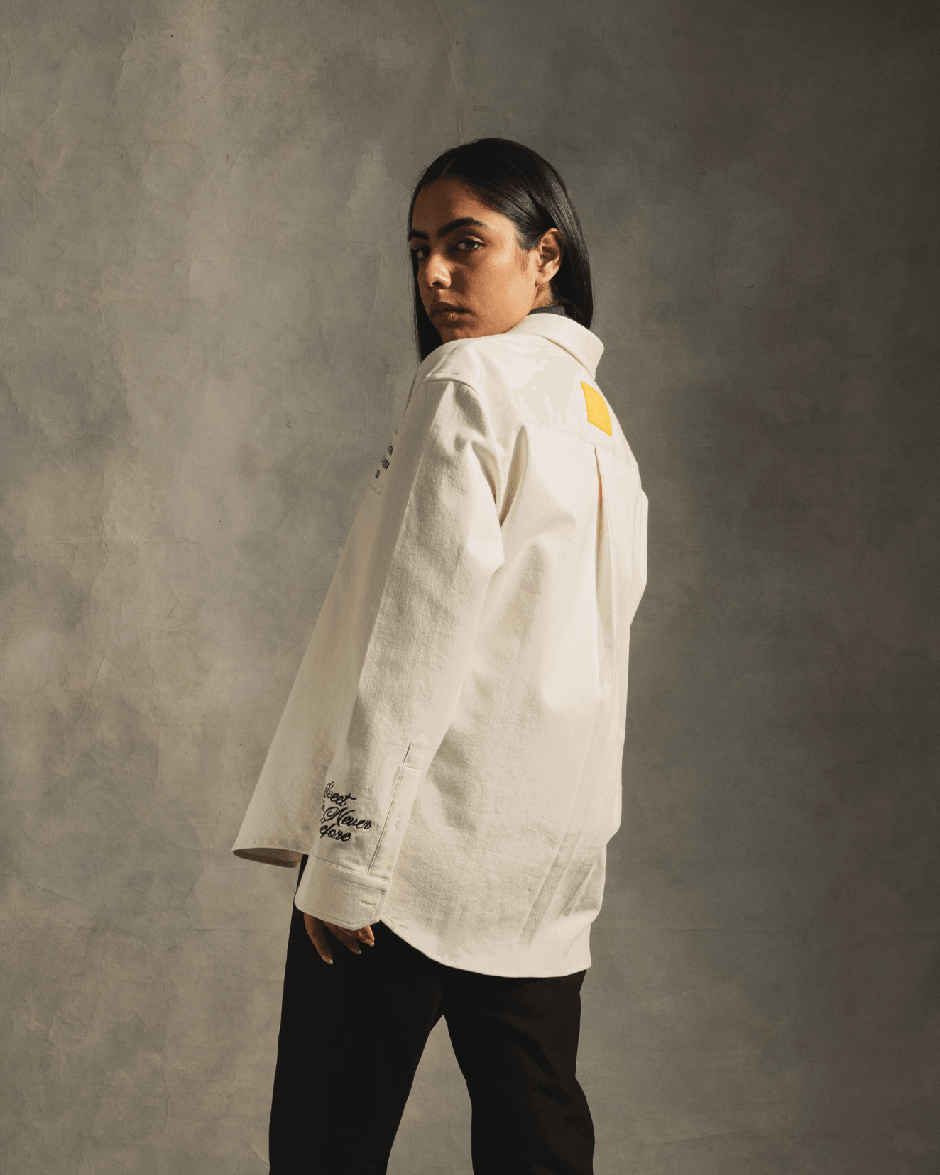 Woman in white oversized streetwear shirt with black pants, standing in studio