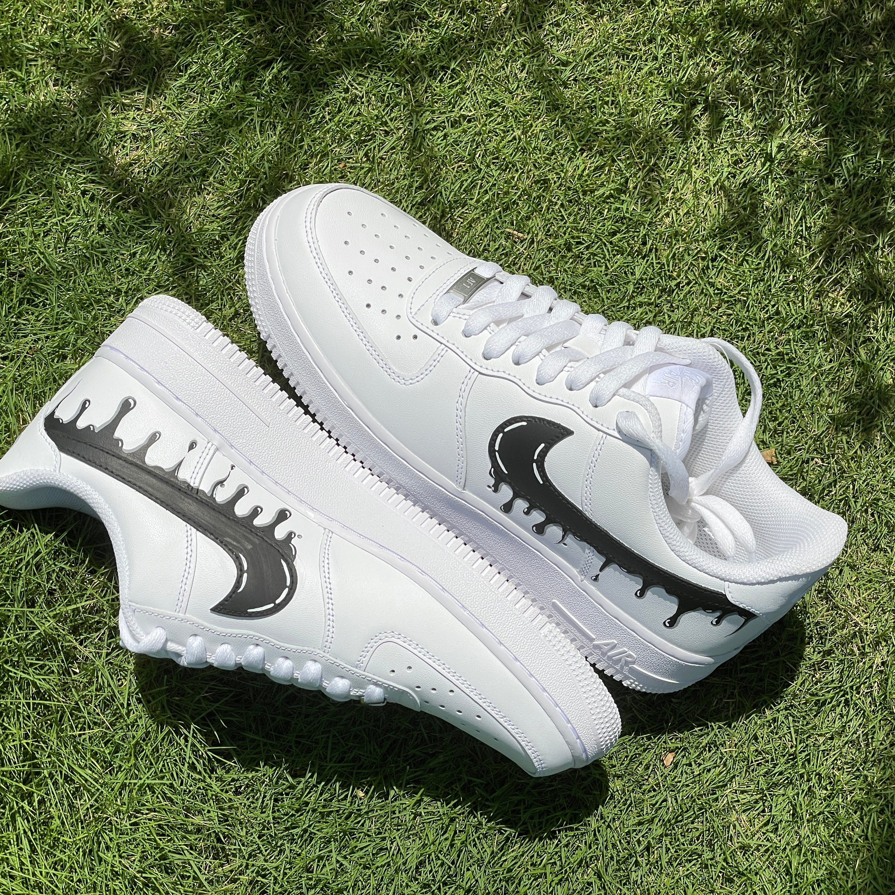 White streetwear sneakers with black drip swoosh logo on green grass outdoors