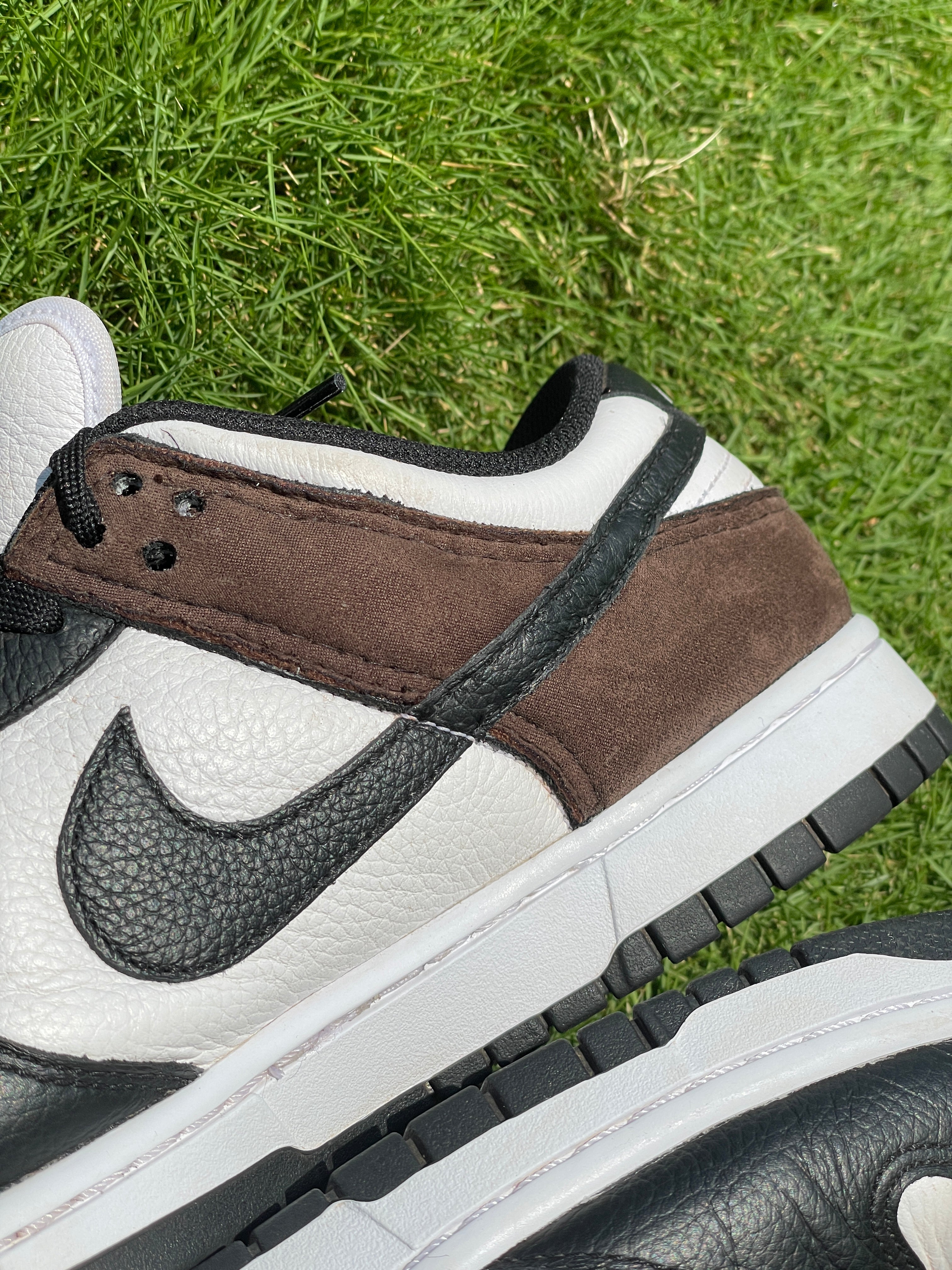 Close-up of black, white, and brown leather low-top sneaker on grass