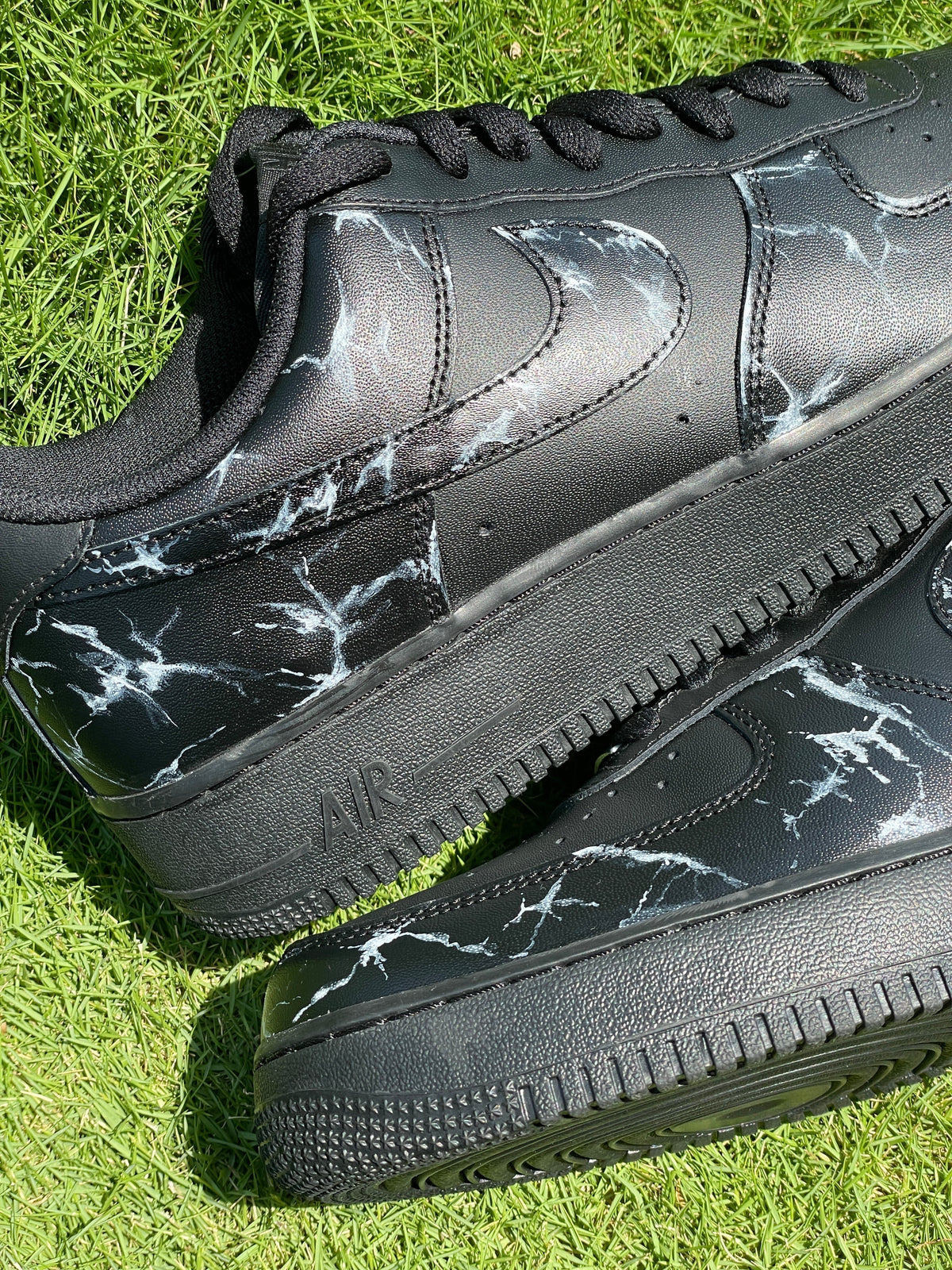 Black streetwear sneakers with white marble pattern on grass, trendy designer footwear