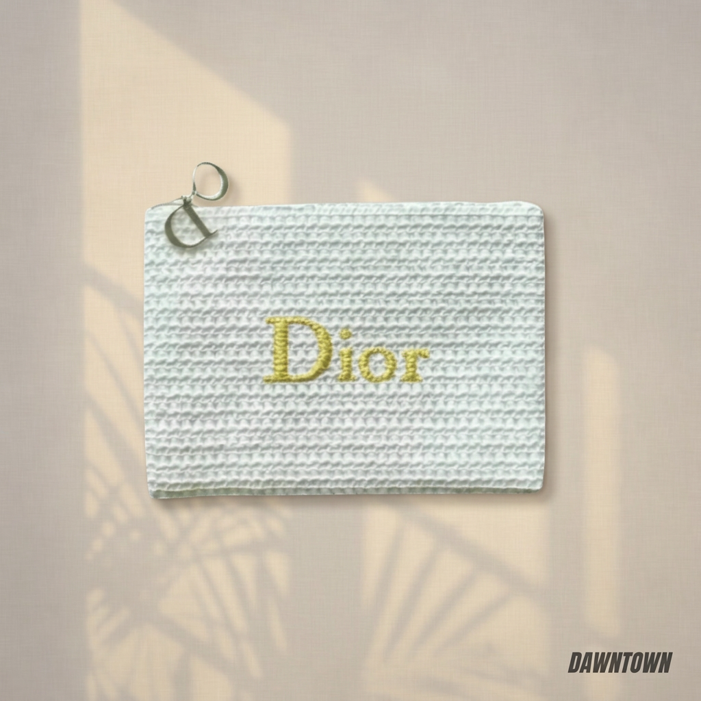 White textured Dior pouch with gold lettering on a softly lit ivory background