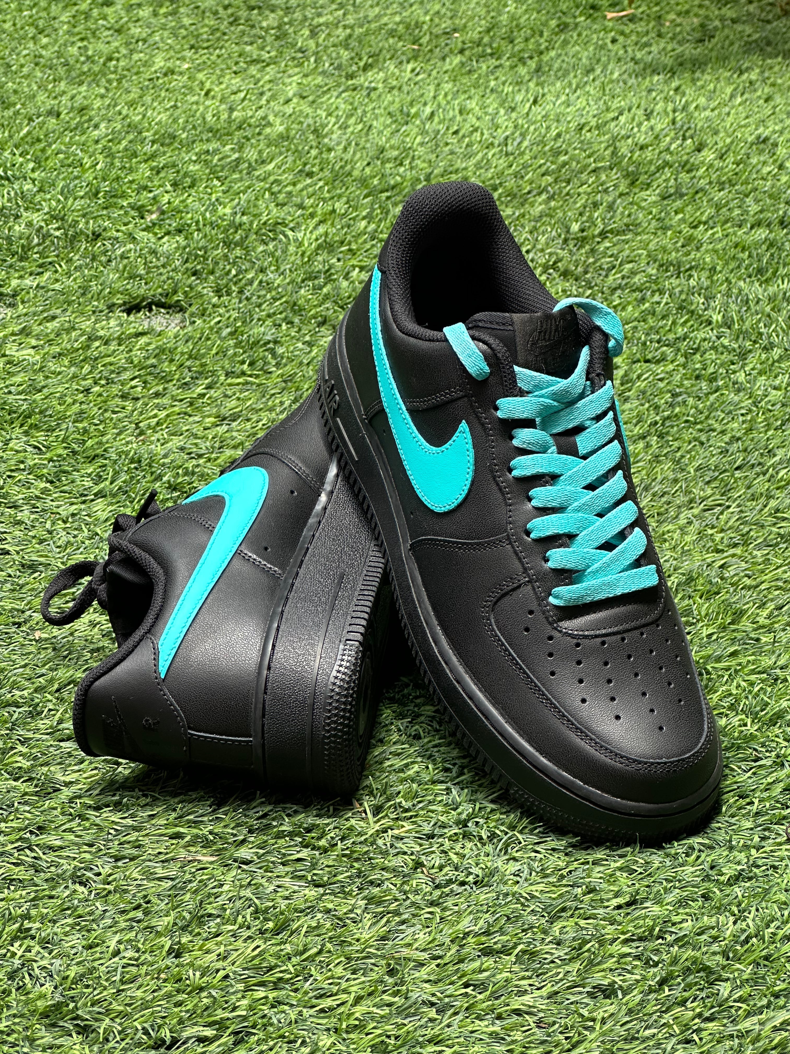 Black Nike Air Force 1 sneakers with turquoise swoosh and laces on grass