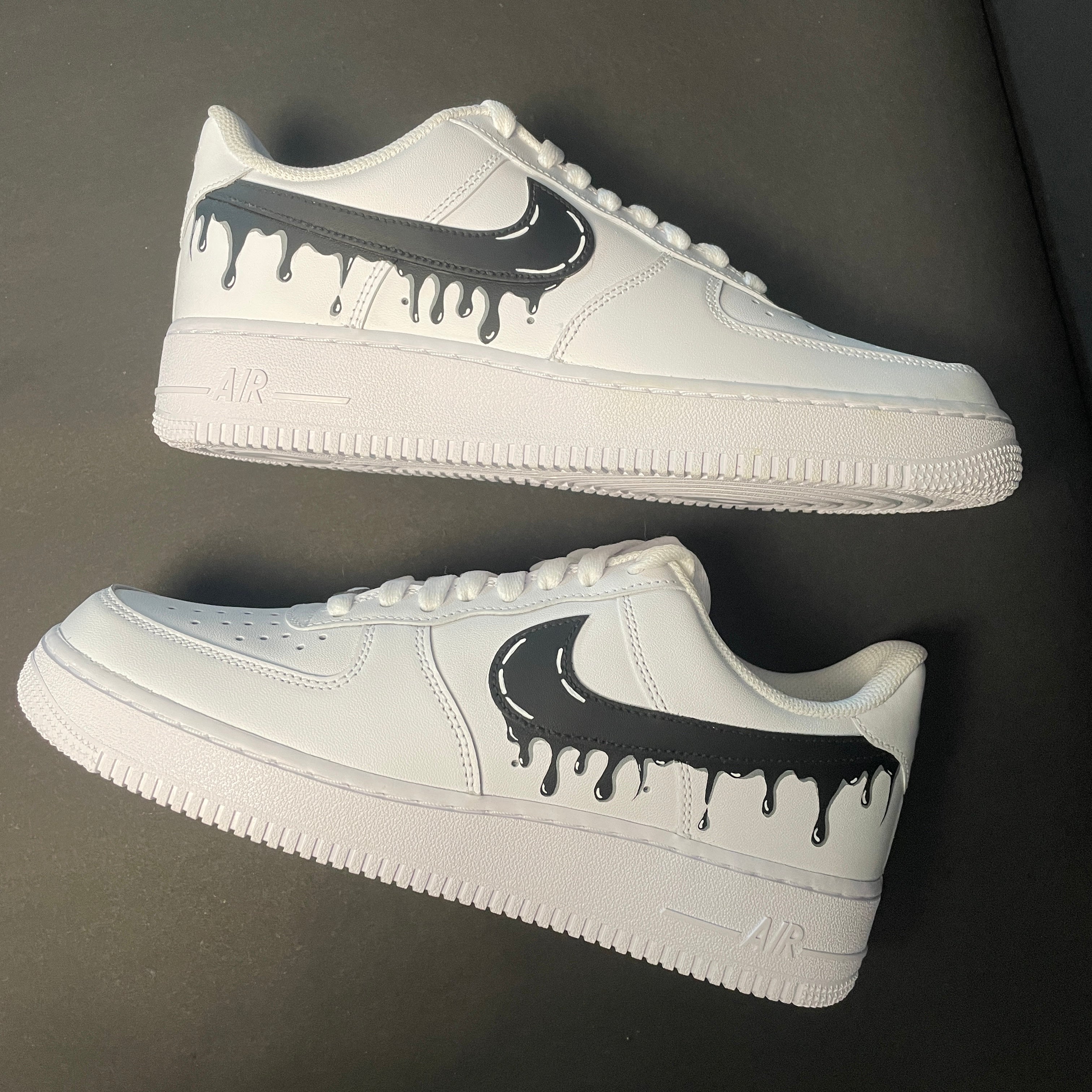 White low-top streetwear sneakers with black drip Swoosh design on side, luxury footwear