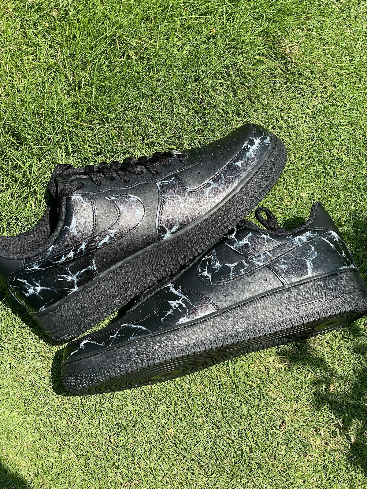 Black streetwear sneakers with white marble pattern on grass, designer footwear