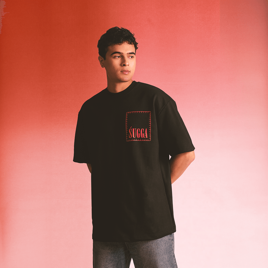 Man wearing black streetwear t-shirt with red 'SUGGA' patch, casual fashion photoshoot