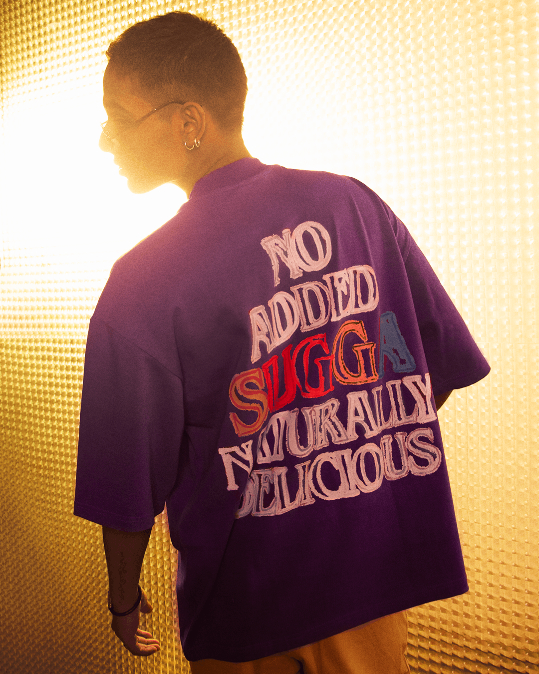 Man wearing purple graphic streetwear t-shirt with bold embroidered text on the back