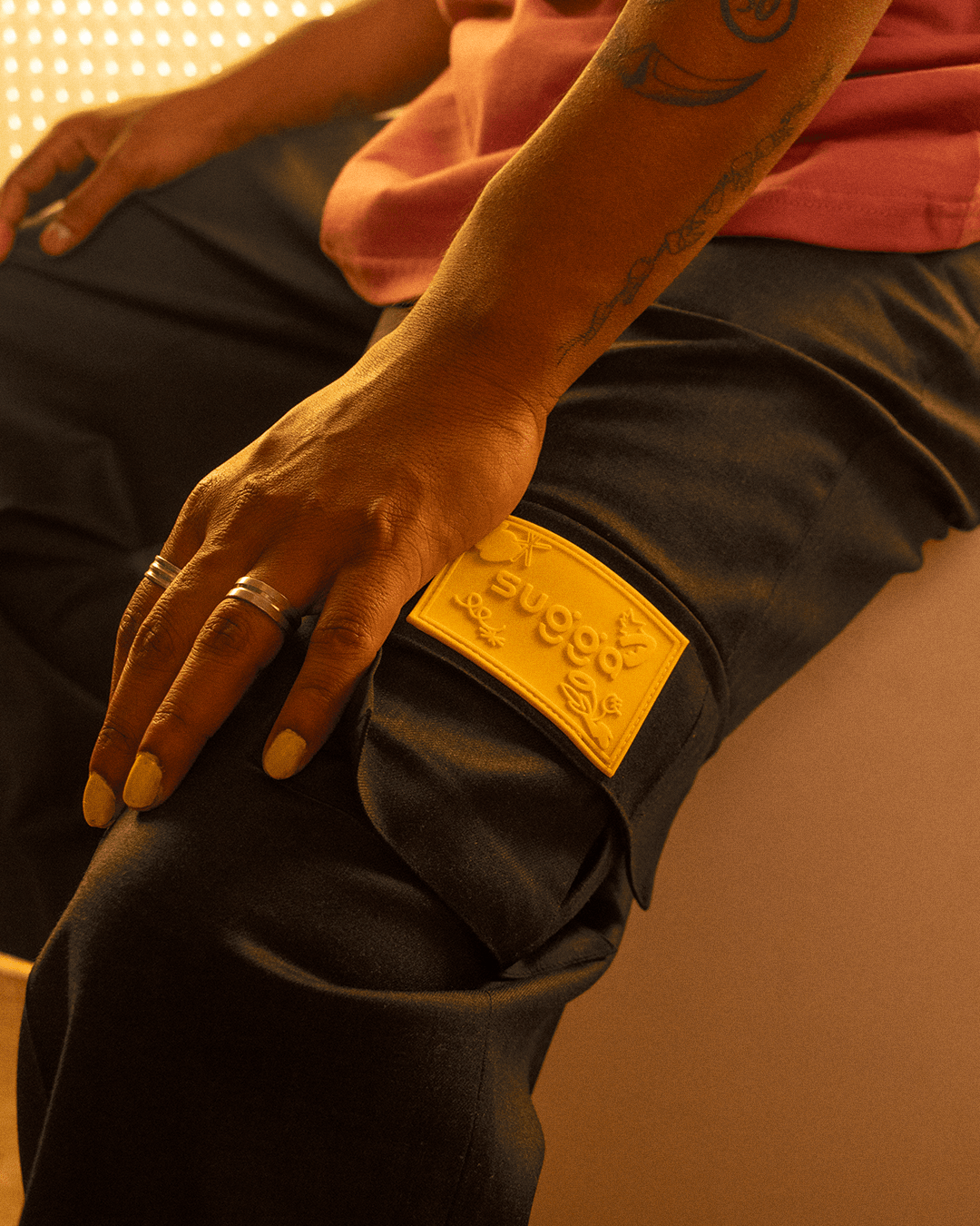 Close-up of black cargo pants with yellow patch, streetwear style, hand resting on thigh