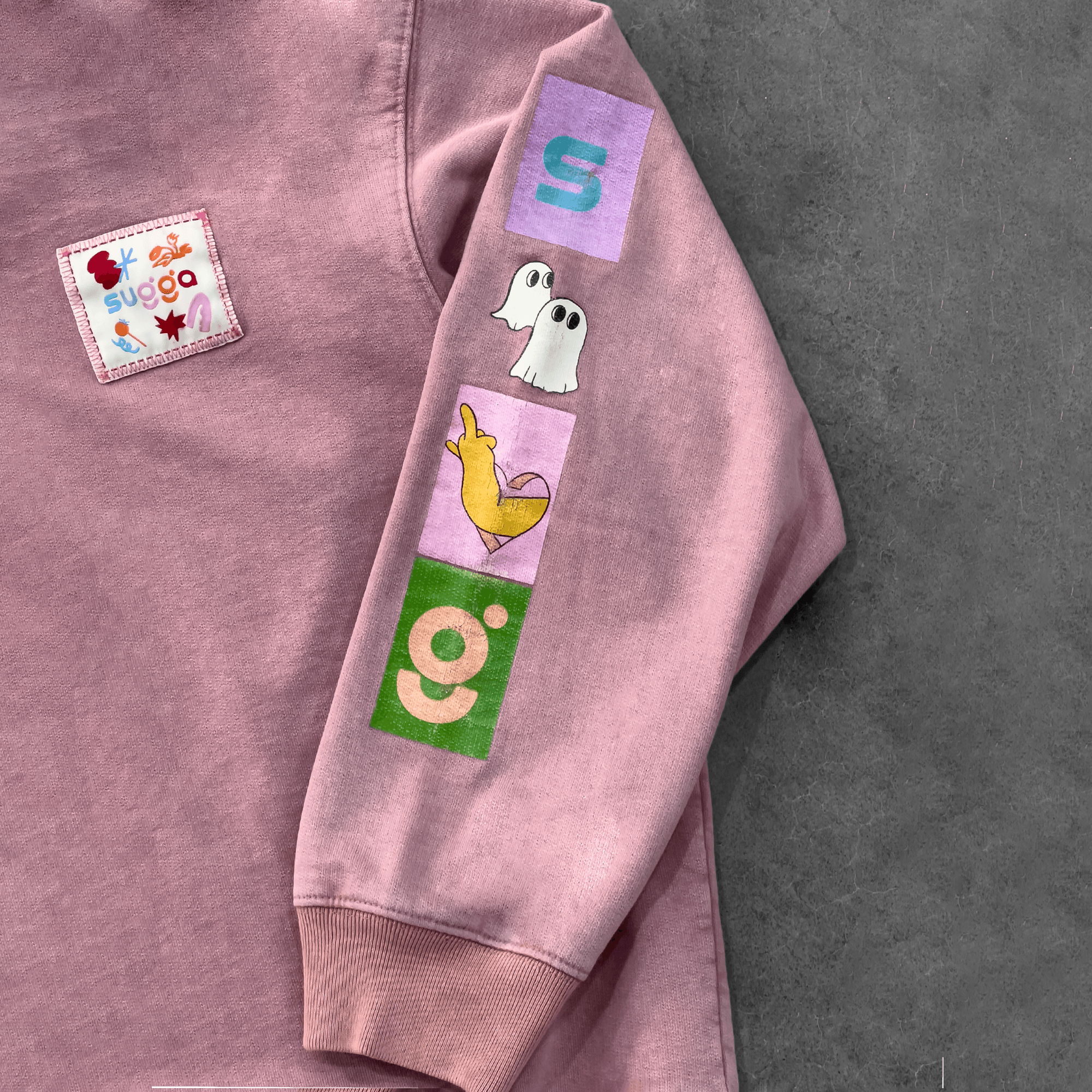 Pink hoodie sleeve with colorful patchwork, ghost and animal graphics, streetwear style