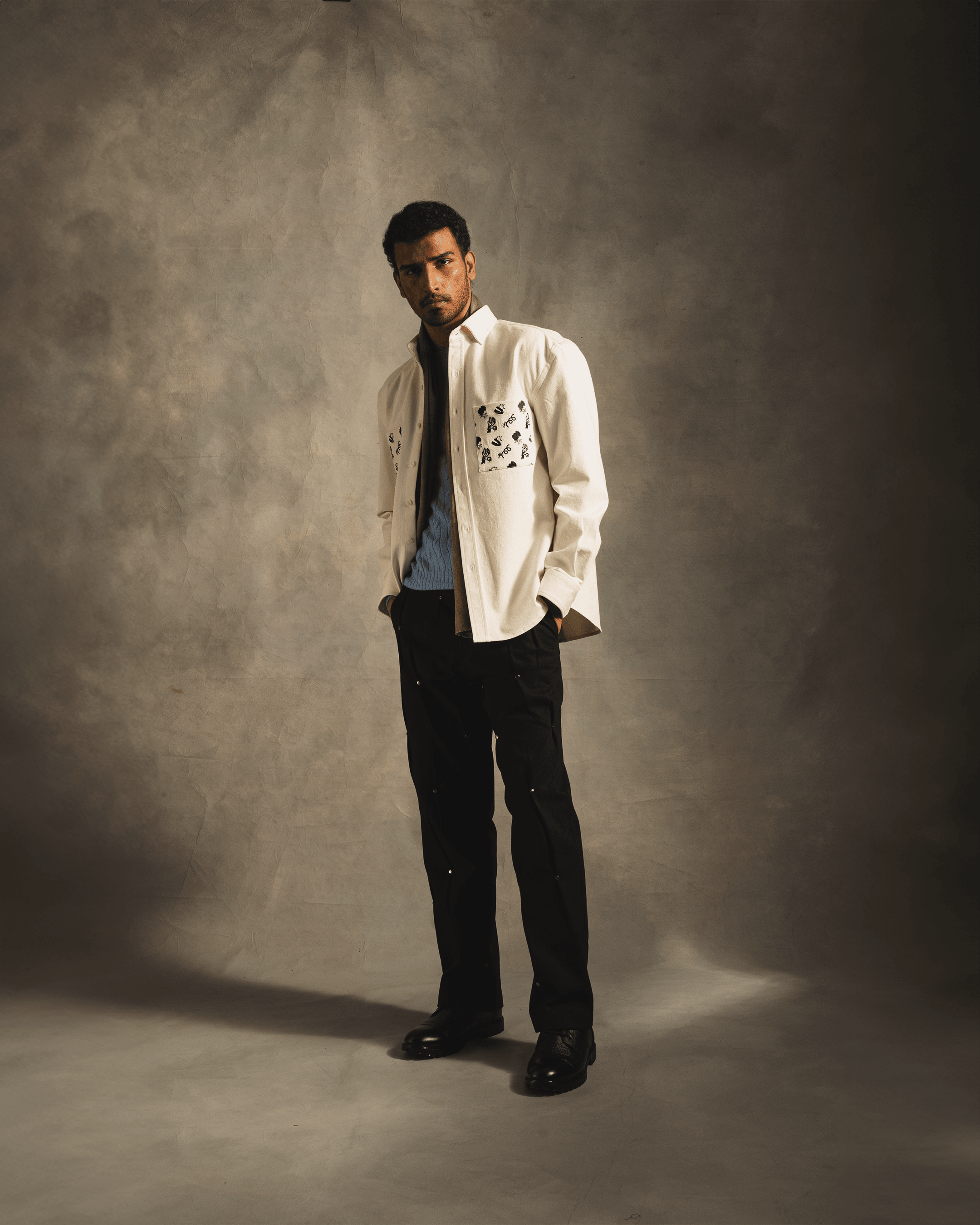 Man modeling streetwear with white embroidered pocket shirt, black pants, and dress shoes