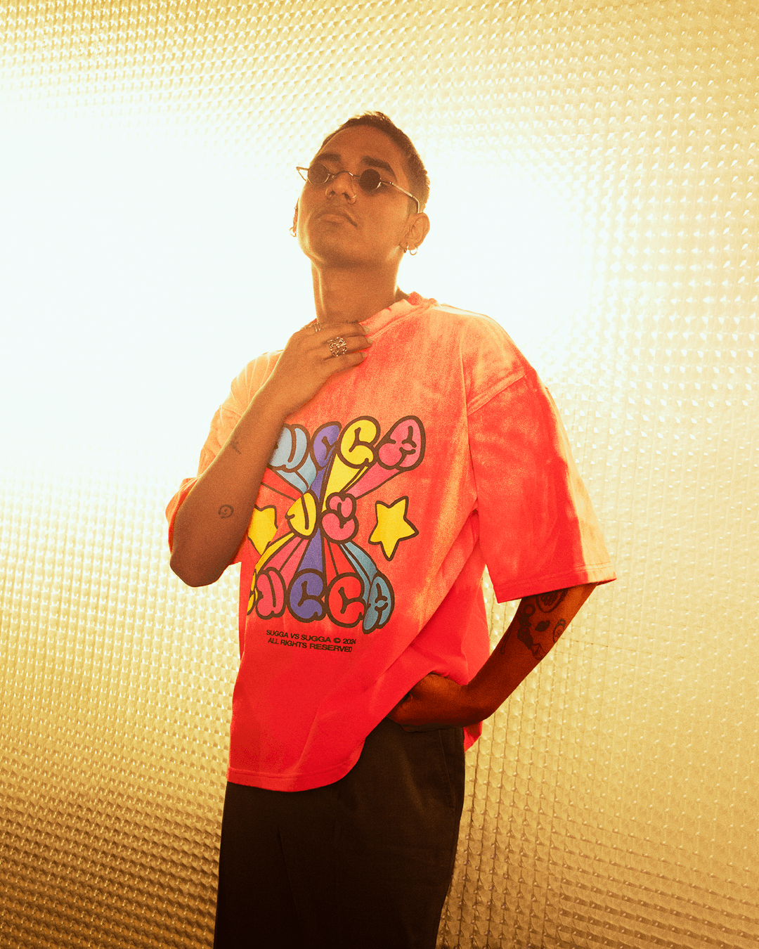 Person wearing bright graphic streetwear T-shirt with colorful stars and text, sunglasses, tattoos