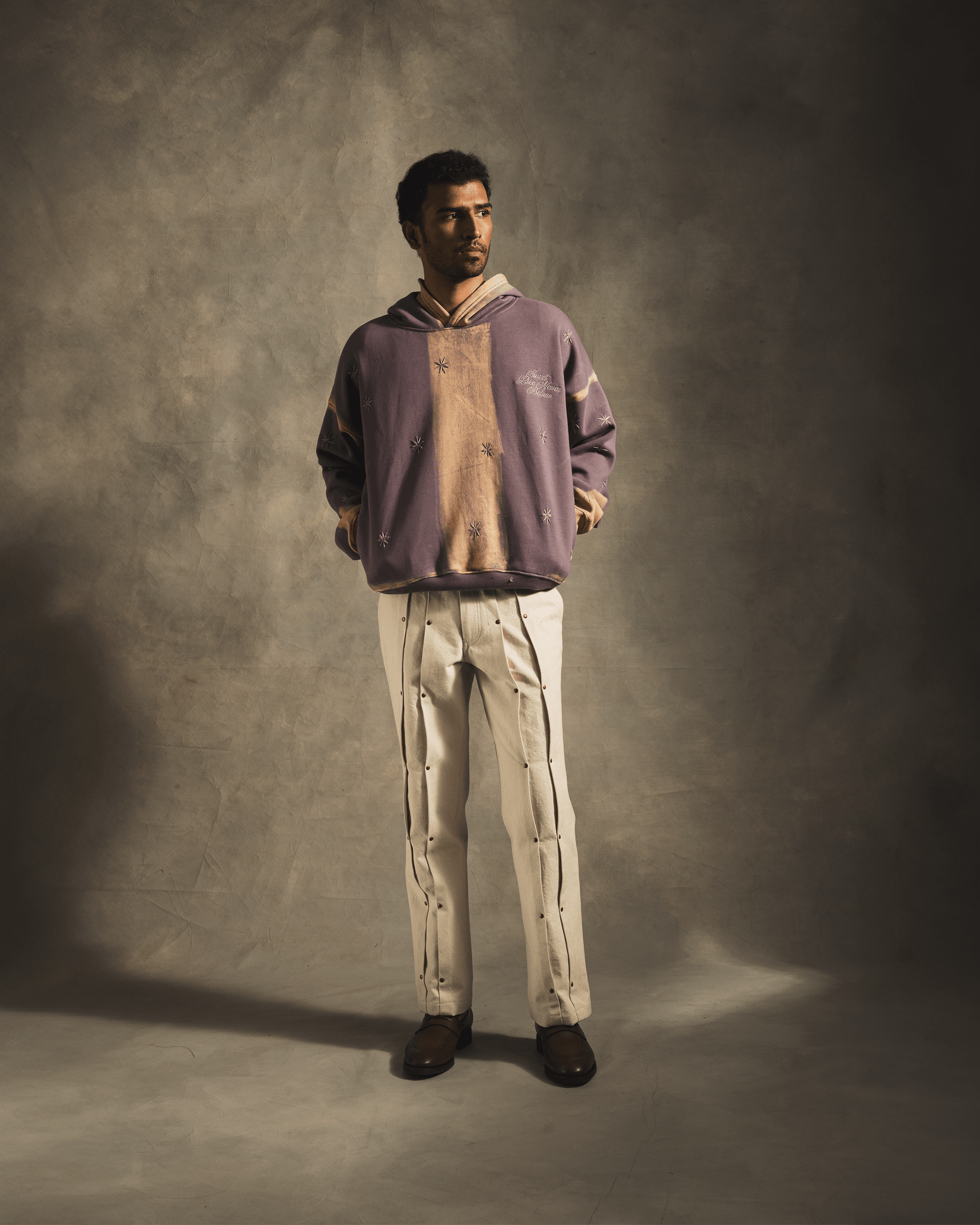 Man in a purple hooded streetwear sweatshirt with patterns and cream designer pants