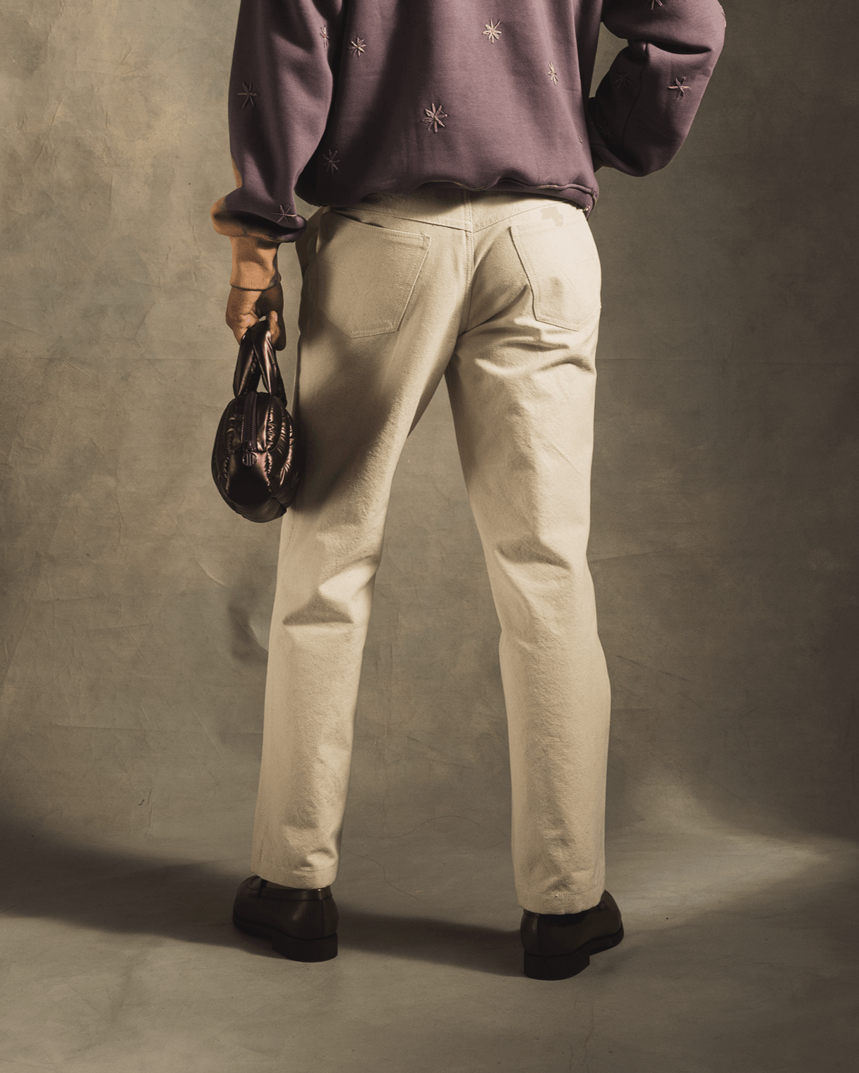 Back view of person in a purple embroidered hoodie and beige pants holding a black bag