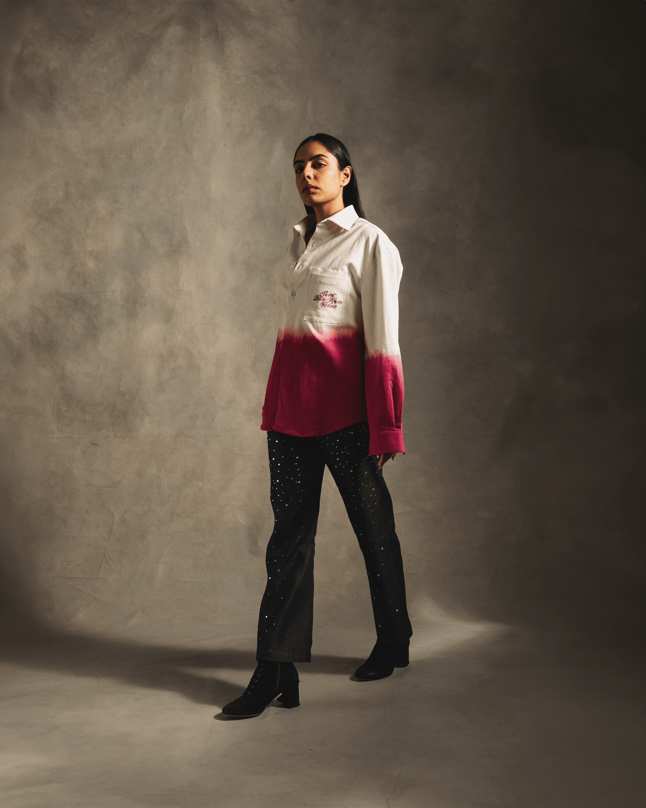 Woman wearing a white and pink dip-dye shirt with black star-studded jeans, indoors