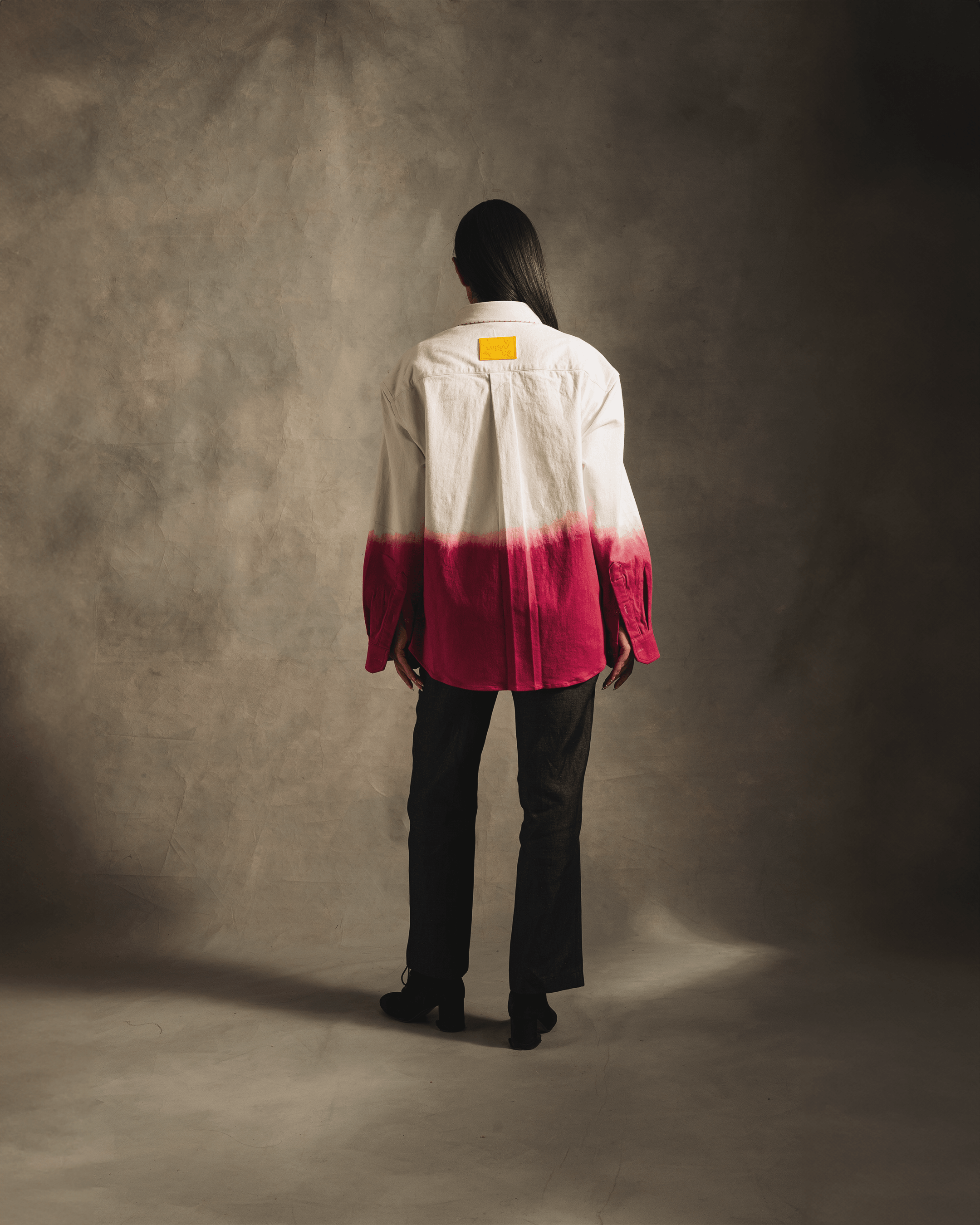 Back view of model in dip-dye pink and white oversized shirt with black jeans, studio setting