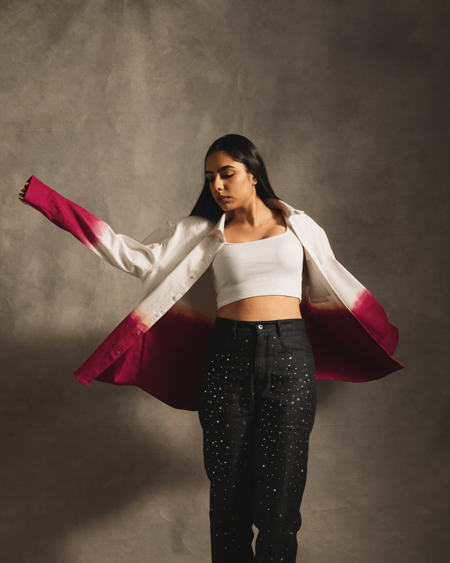 Woman in a white crop top, dark star-studded jeans, and white-pink gradient jacket, streetwear style