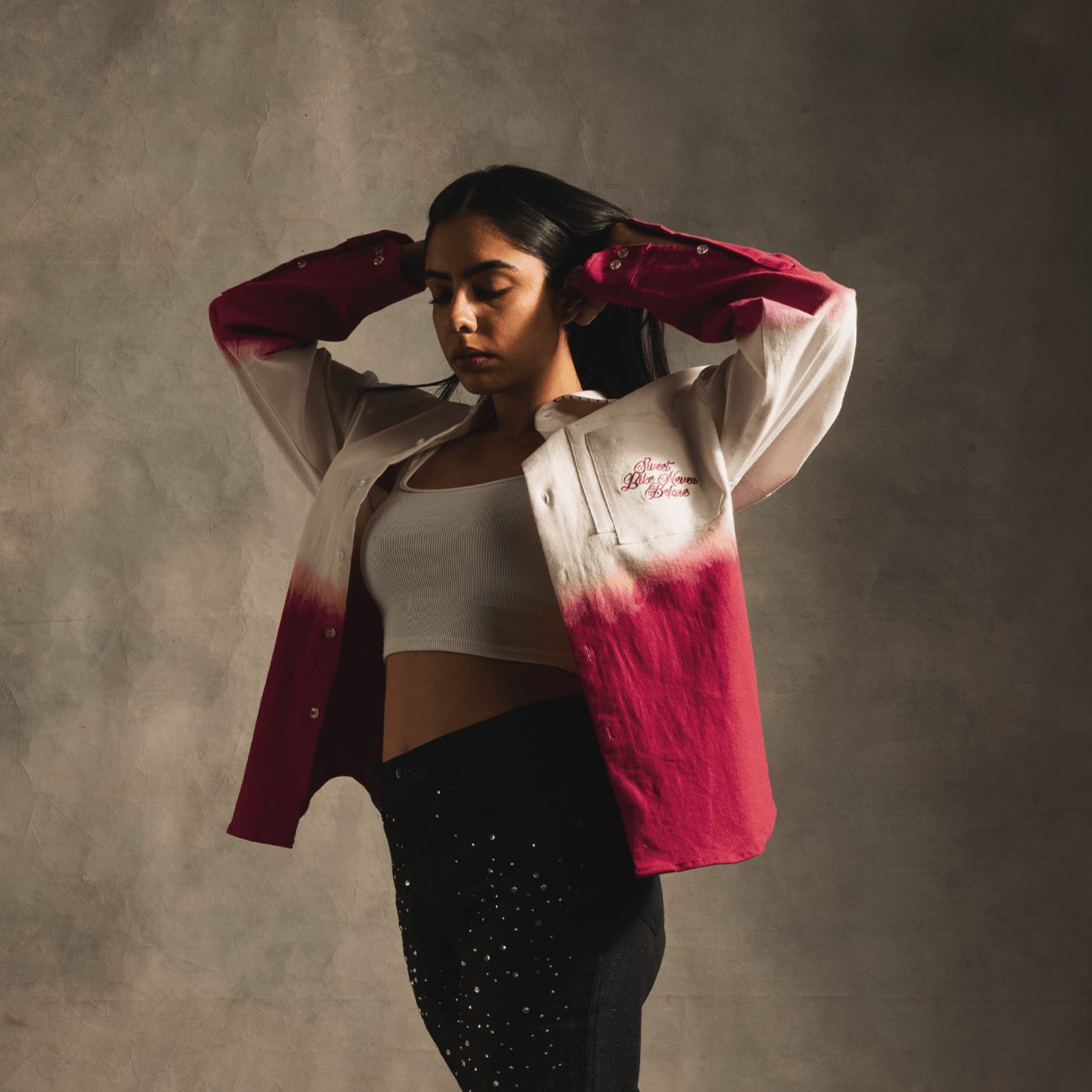 Woman wearing pink gradient button-up shirt, white crop top, and star-studded black jeans