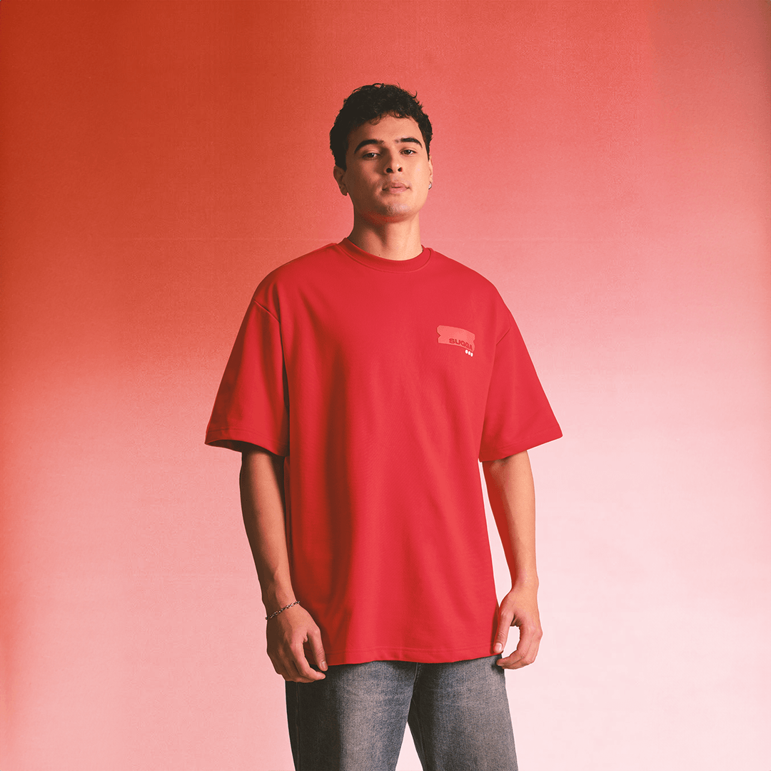 Man wearing loose red oversized streetwear t-shirt with small chest logo, casual jeans