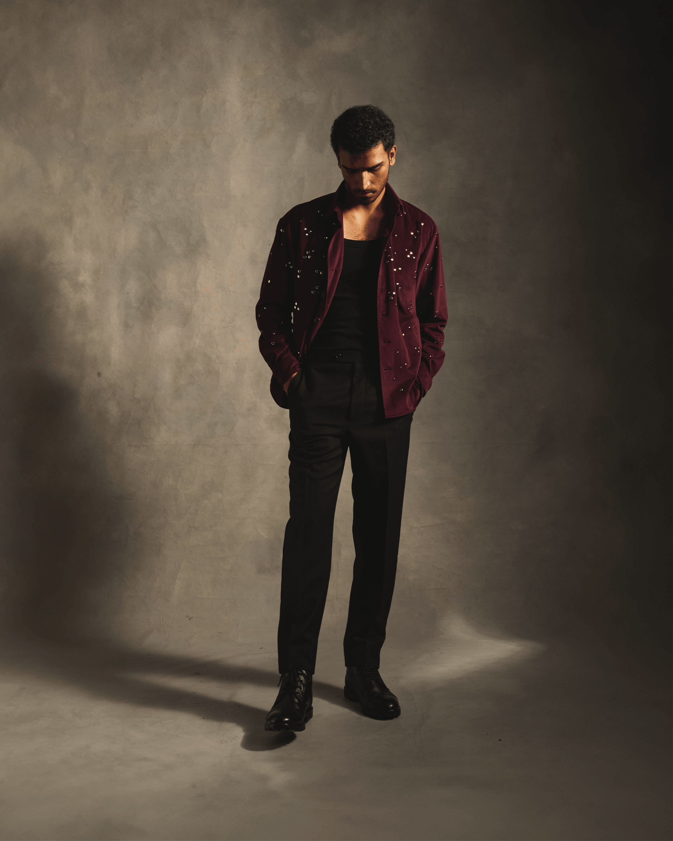 Man wearing a red velvet studded shirt with black pants and dress shoes in studio lighting