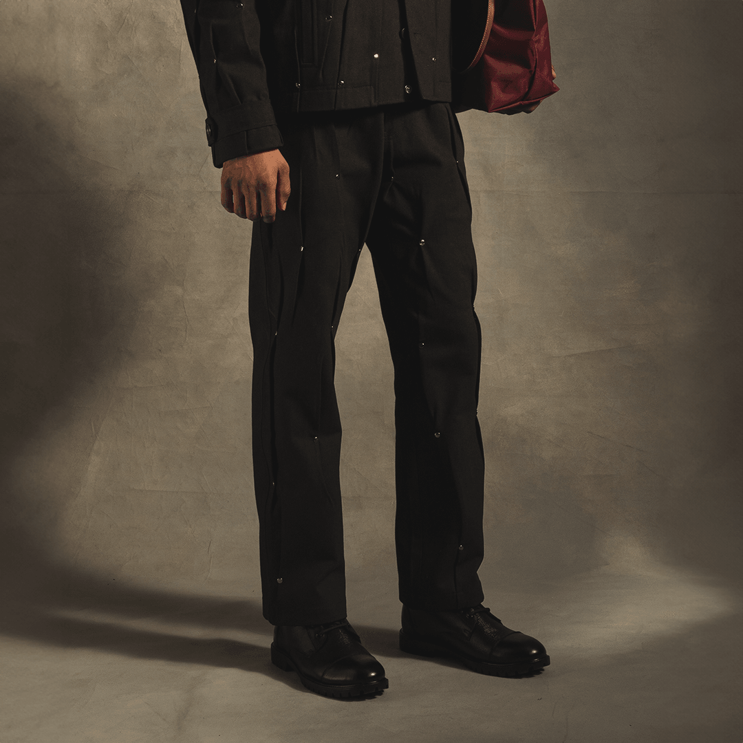 Man wearing black streetwear jeans with rivet accents and black shoes in studio setting
