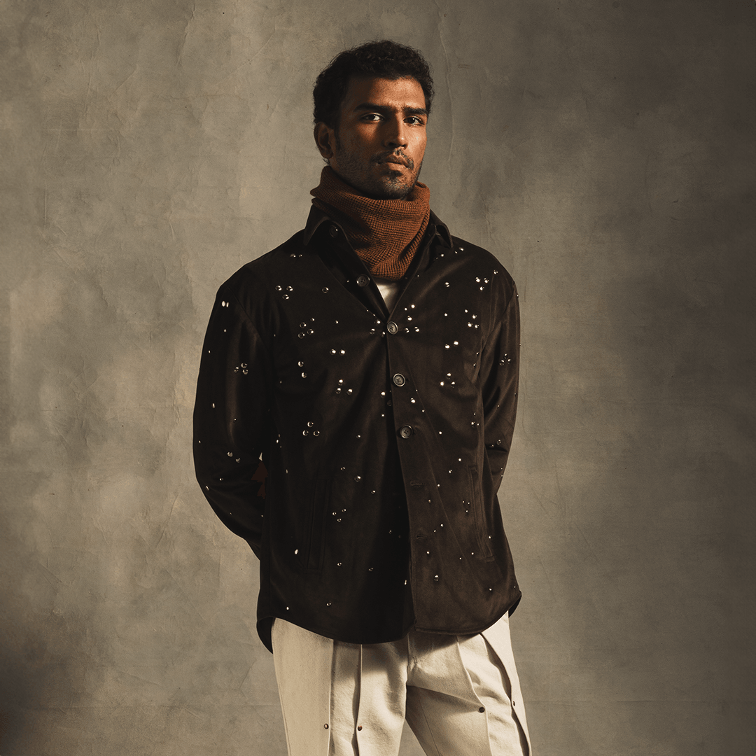 Man modeling a black rivet-embellished streetwear shirt and light pants against a neutral background