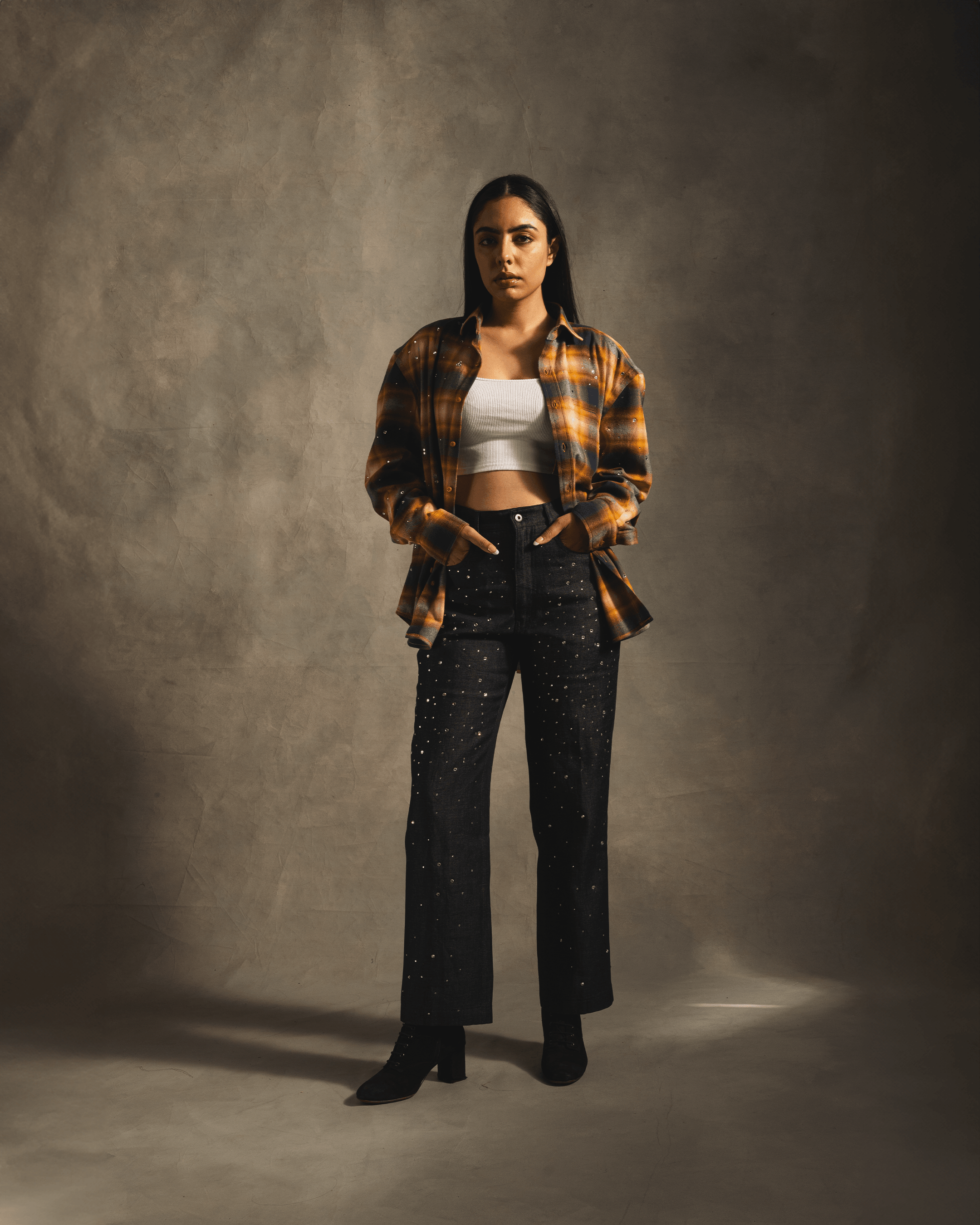 Woman wearing yellow plaid flannel shirt, white crop top, and studded black jeans, streetwear style