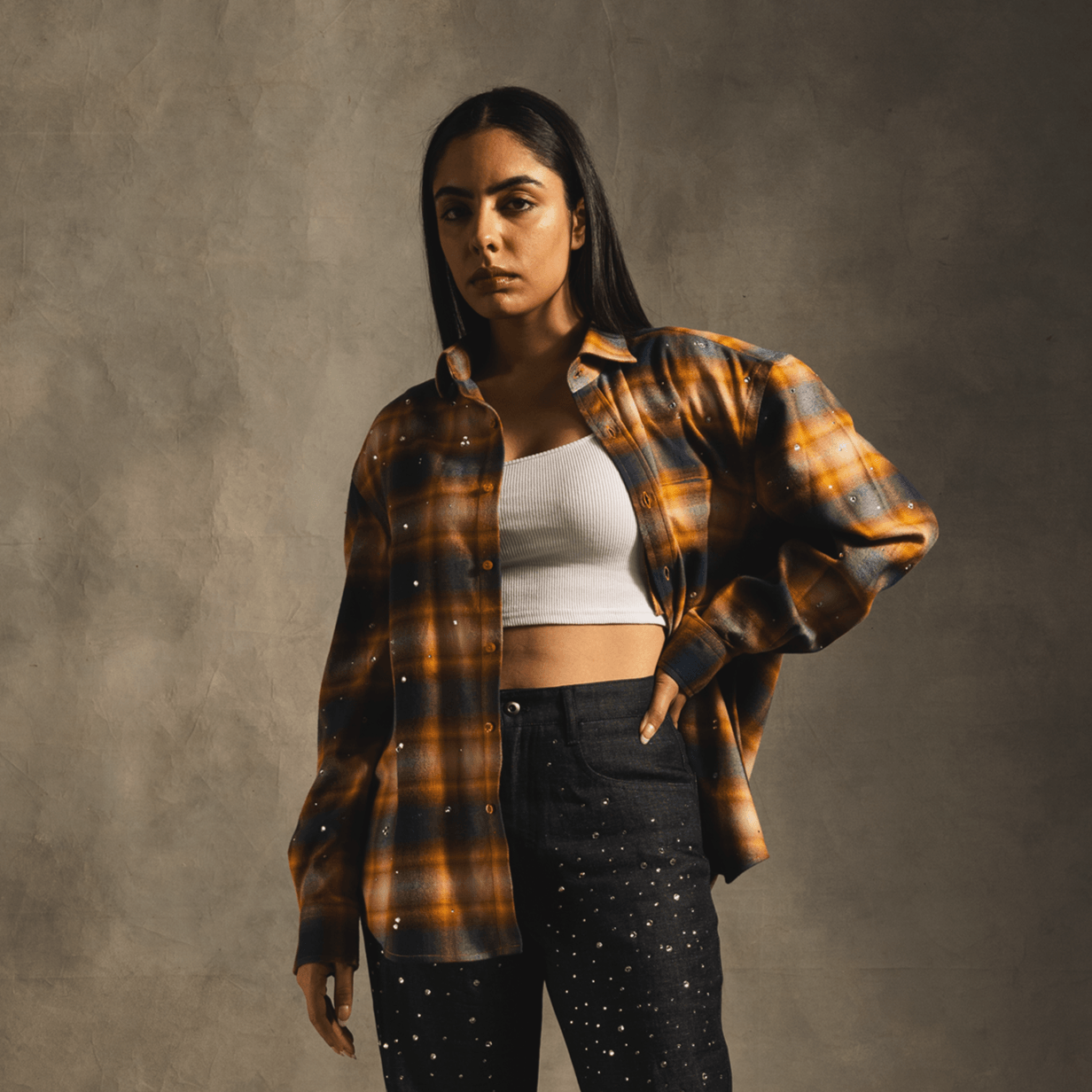 Woman wearing orange plaid flannel shirt, white crop top, and black studded jeans, streetwear style