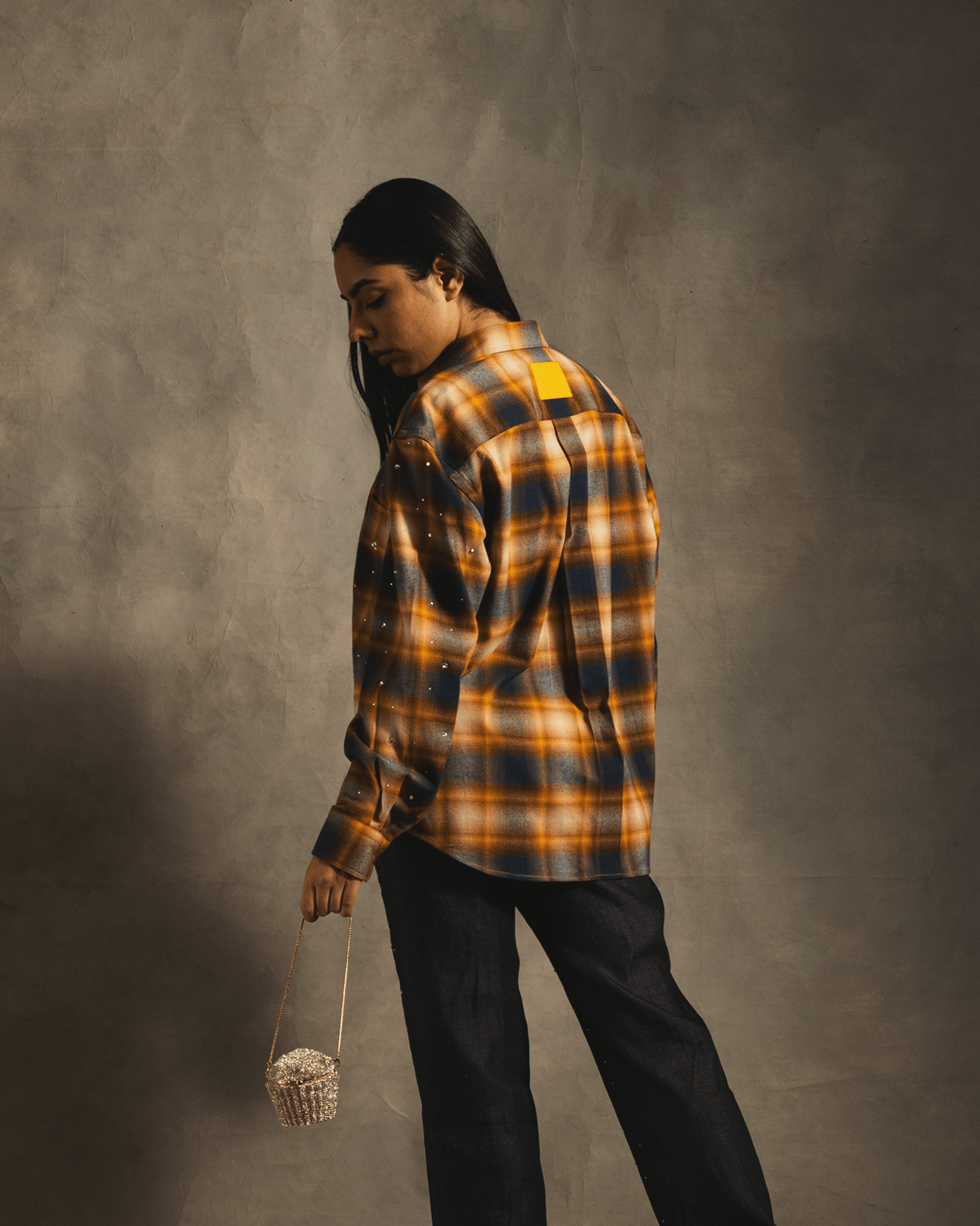 Model wearing oversized plaid flannel shirt with rhinestone accents and holding beaded bag