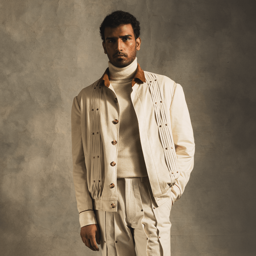 Man wearing cream suede streetwear jacket and pants with brown collar, neutral background