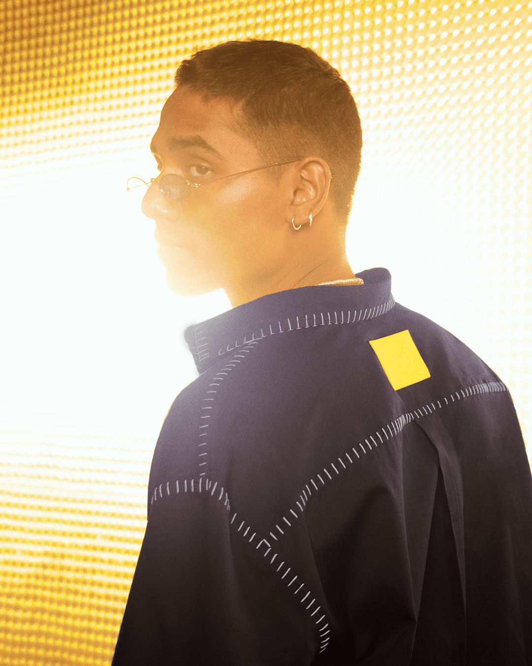 Man in trendy streetwear jacket with white stitching and yellow patch, gold background