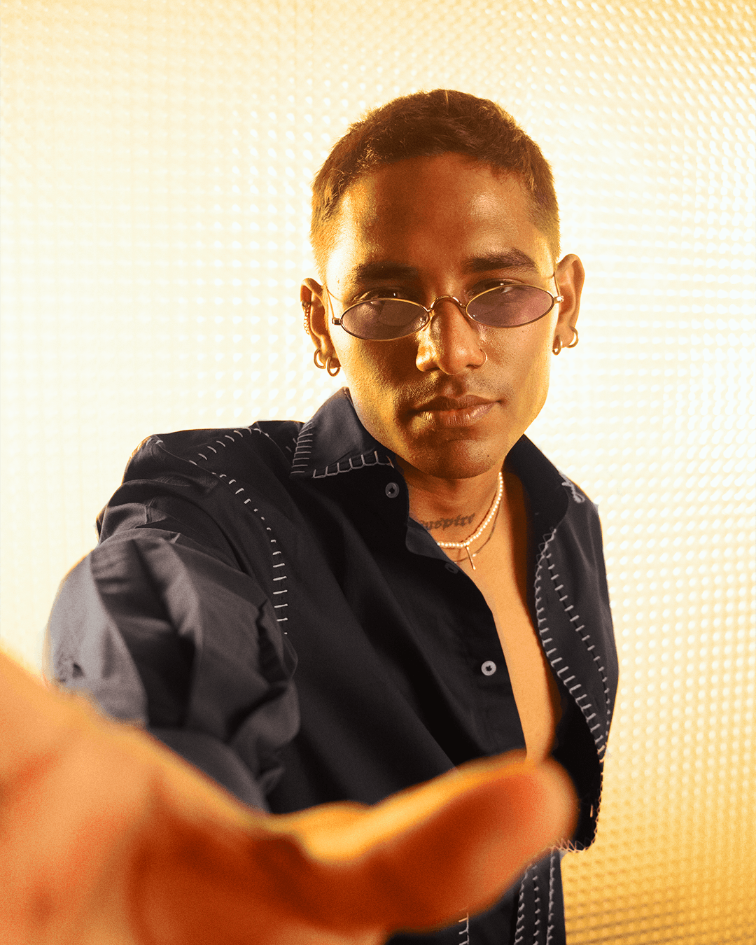 Man in streetwear shirt and sunglasses posing with hand forward, gold textured background
