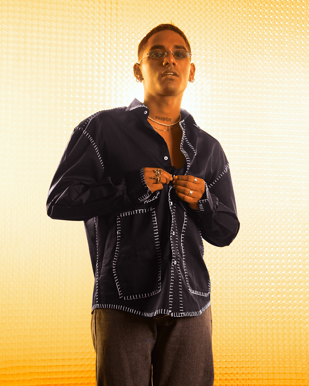 Man wearing dark streetwear button-up shirt with contrast stitching, yellow background