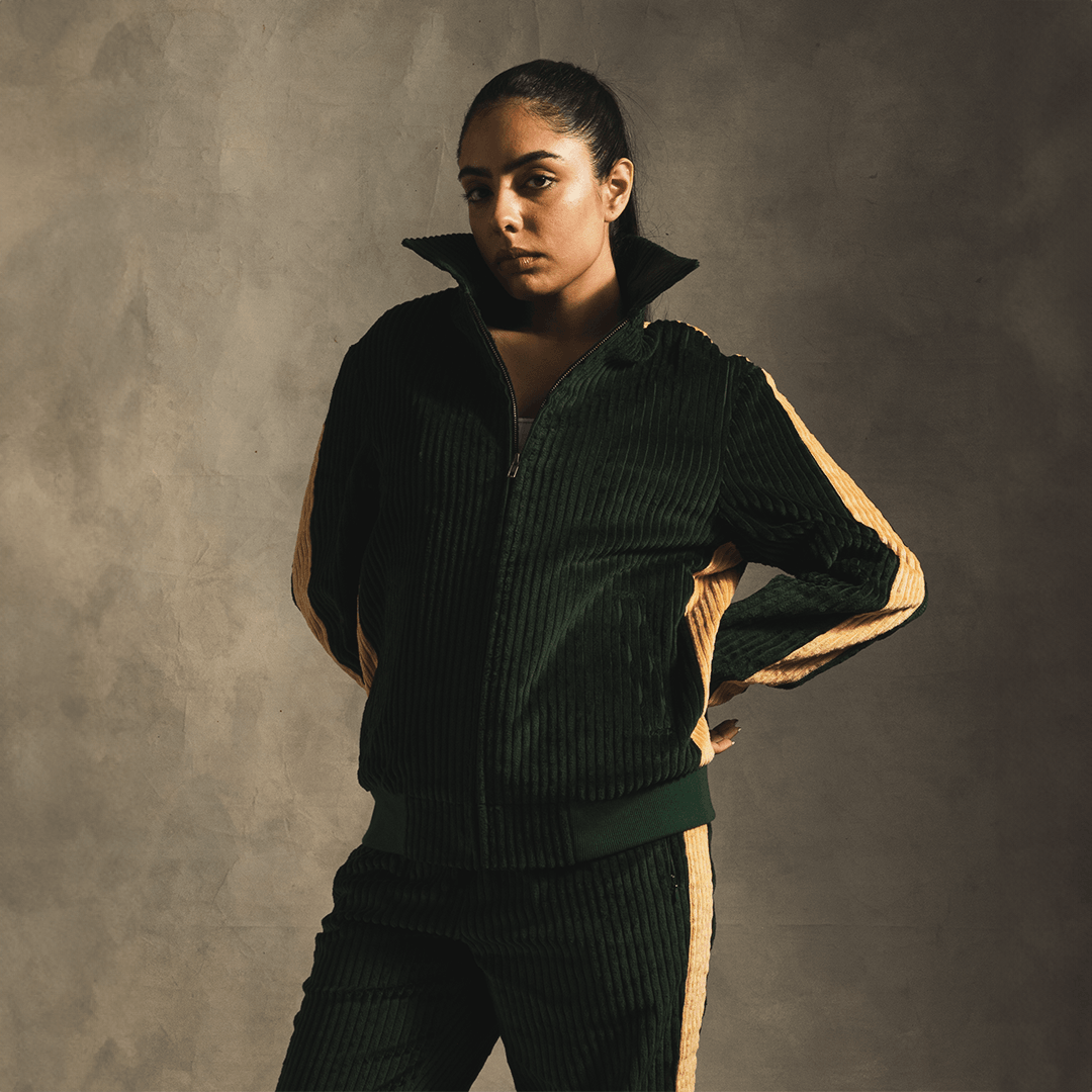 Woman wearing green corduroy track jacket and pants with tan side stripes, streetwear style