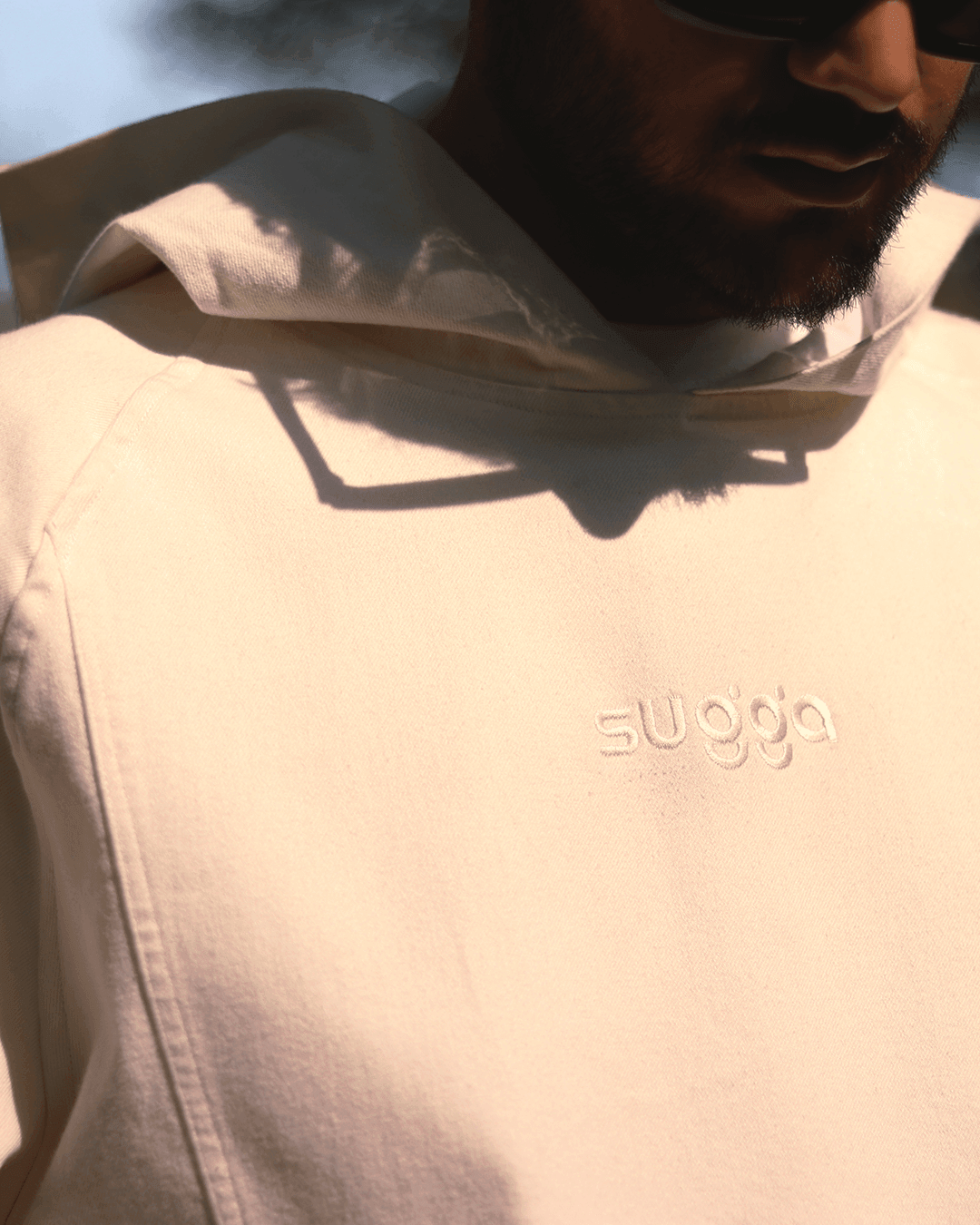 Close-up of a cream white hoodie with subtle 'sugga' embroidered on chest, streetwear style