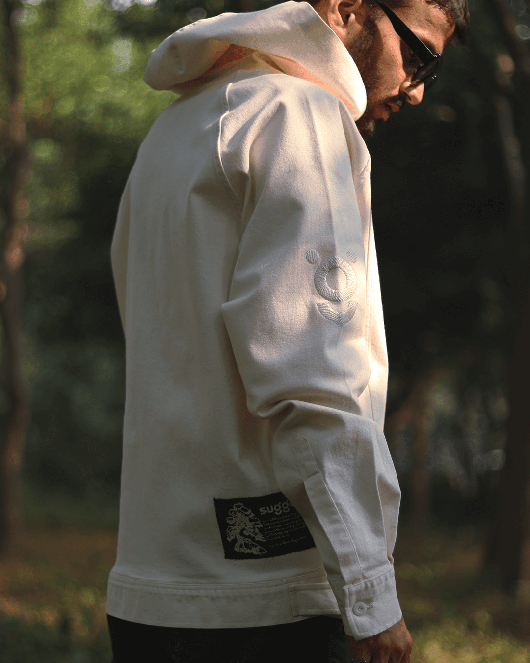 Man wearing a white streetwear hoodie with subtle sleeve embroidery, outdoors in sunlight