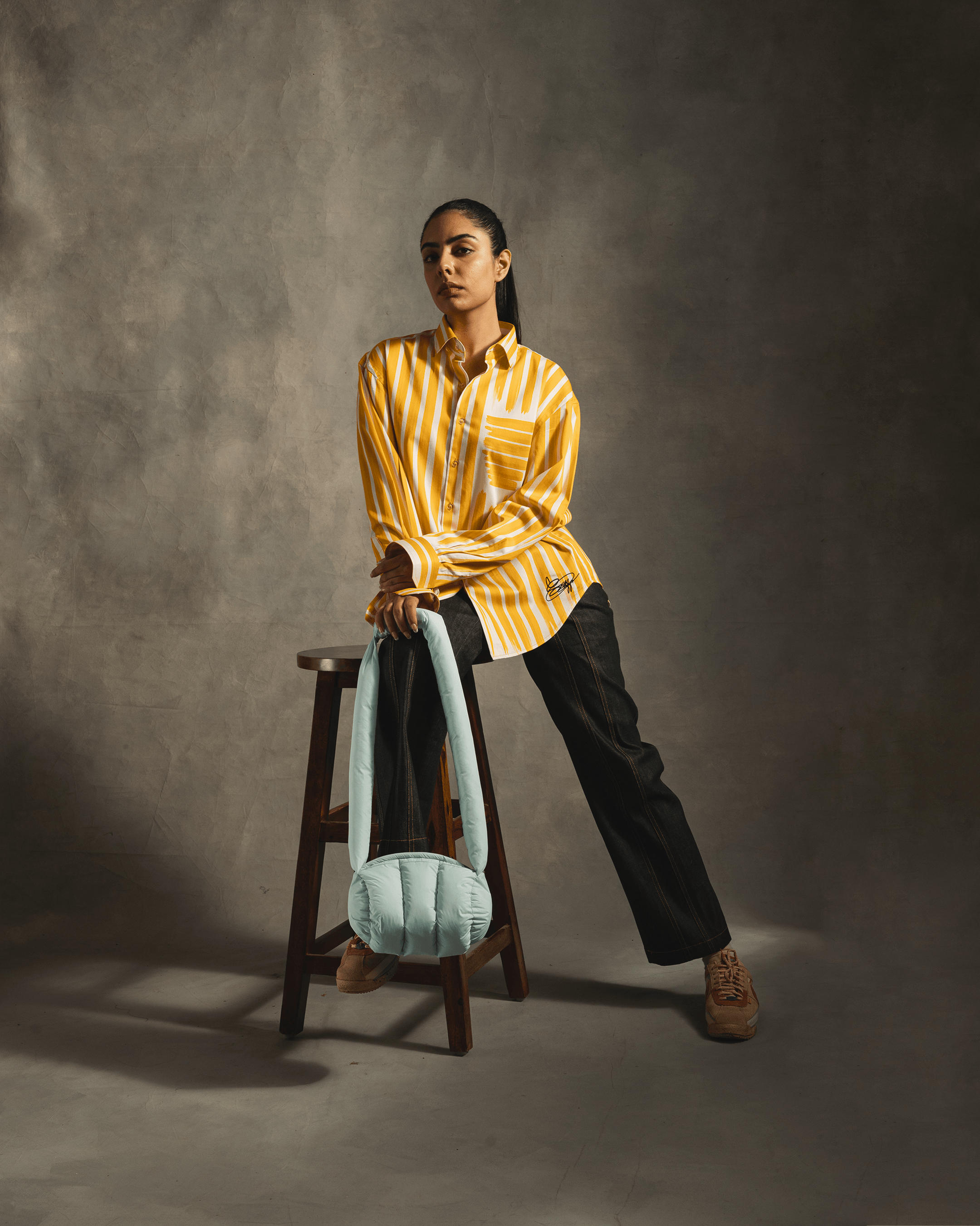 Woman in yellow striped shirt and black pants, holding light blue purse, trendy streetwear style