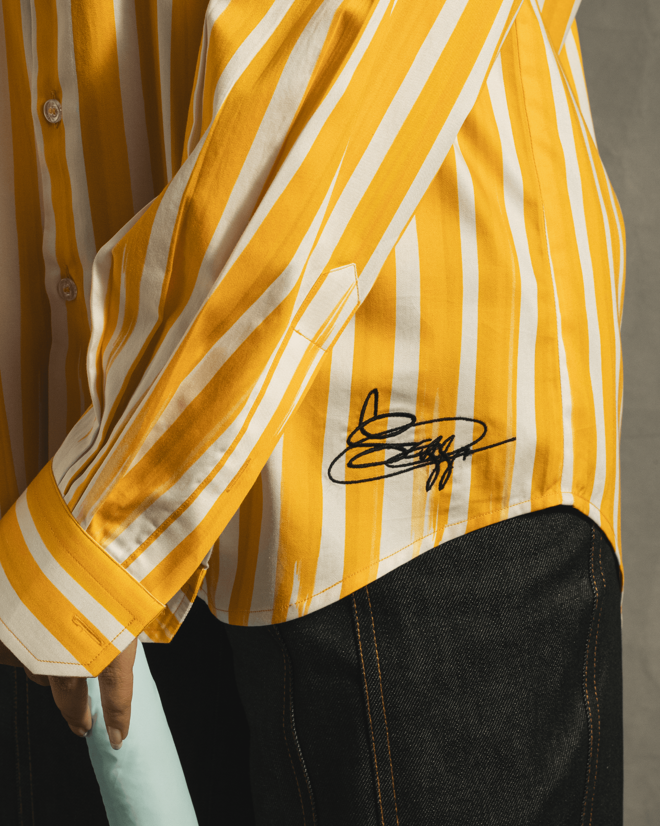 Yellow and white vertical striped shirt with black signature detail, paired with dark denim jeans