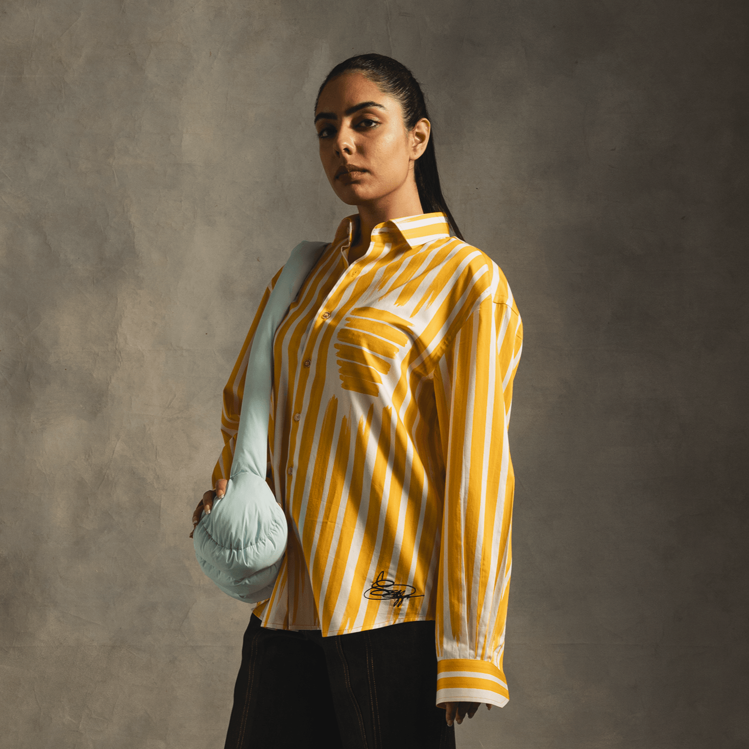 Woman wearing yellow and white striped streetwear shirt, mint shoulder bag, dark pants